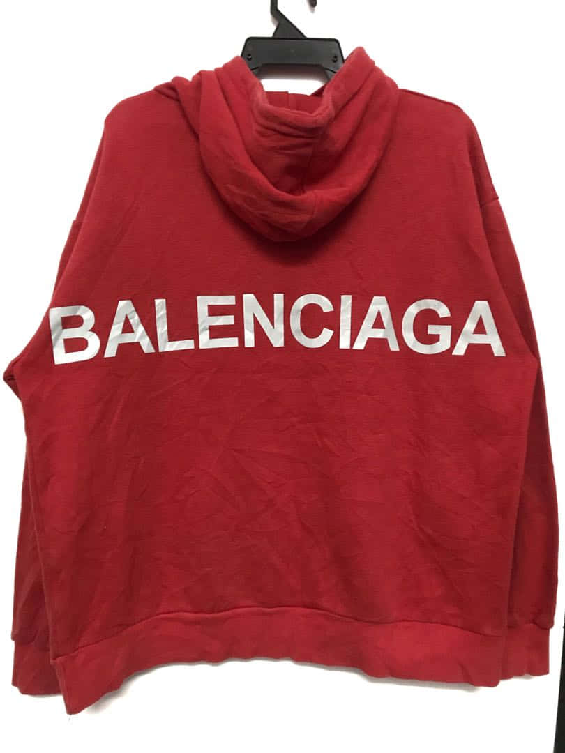 巴黎世家 桌布 壁紙 — 一件紅色 Balenciaga 連帽衛衣，帶有粗體白色標誌，掛在黑色衣架上，背景為純白色。
