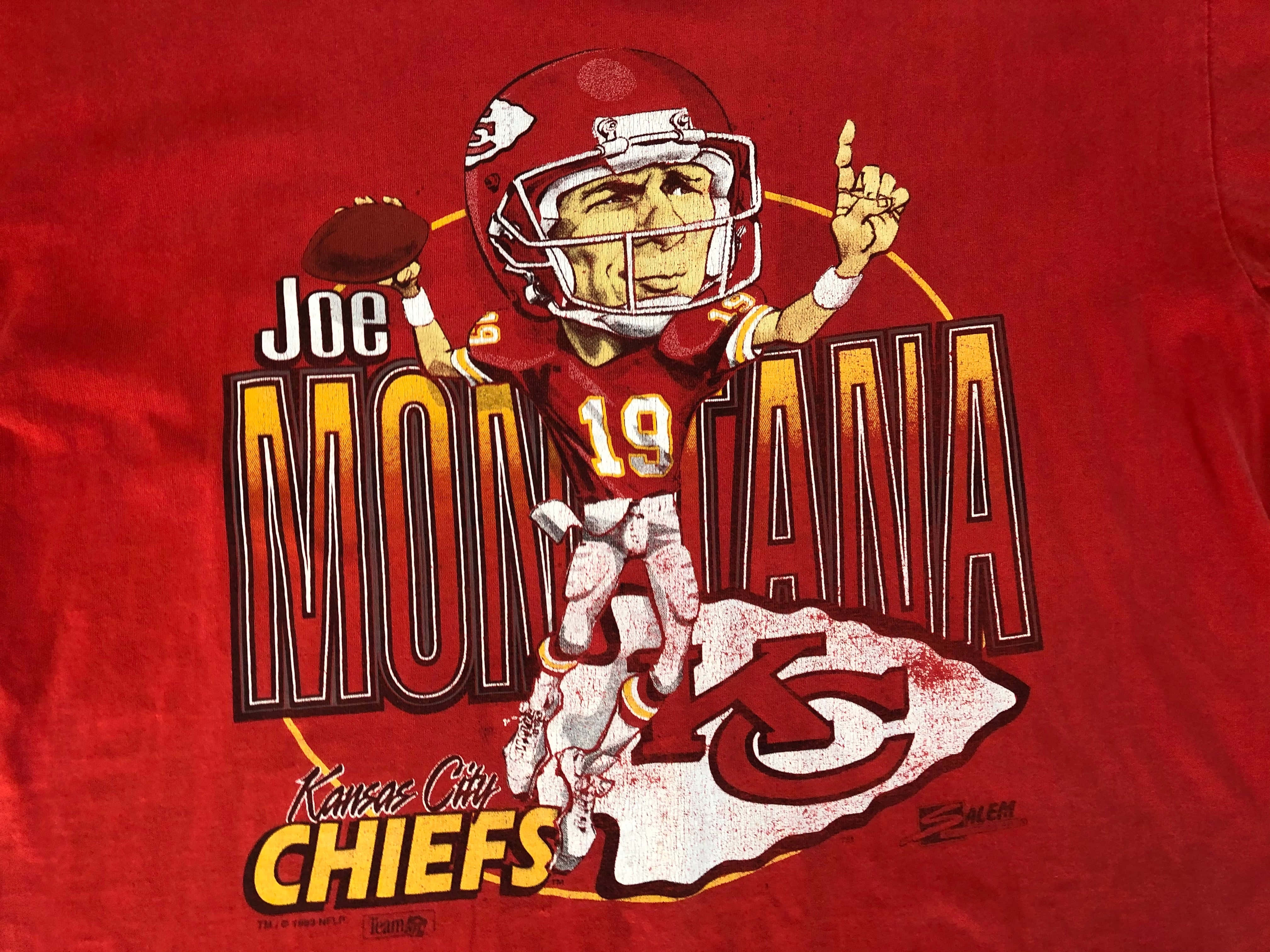 Joe Montana 桌布 壁紙 — 一件紅色T恤上印有喬·蒙塔納穿著酋長隊球衣的卡通漫畫，手持橄欖球並向上指。