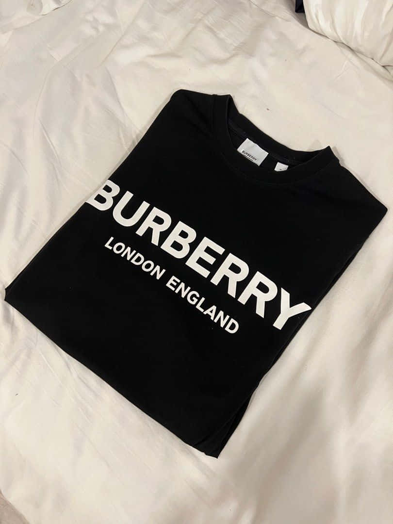 Burberry 桌布 壁紙 — 一件黑色Burberry T恤，上面有粗體白色字樣，整齊地折疊在皺巴巴的白色床單上。