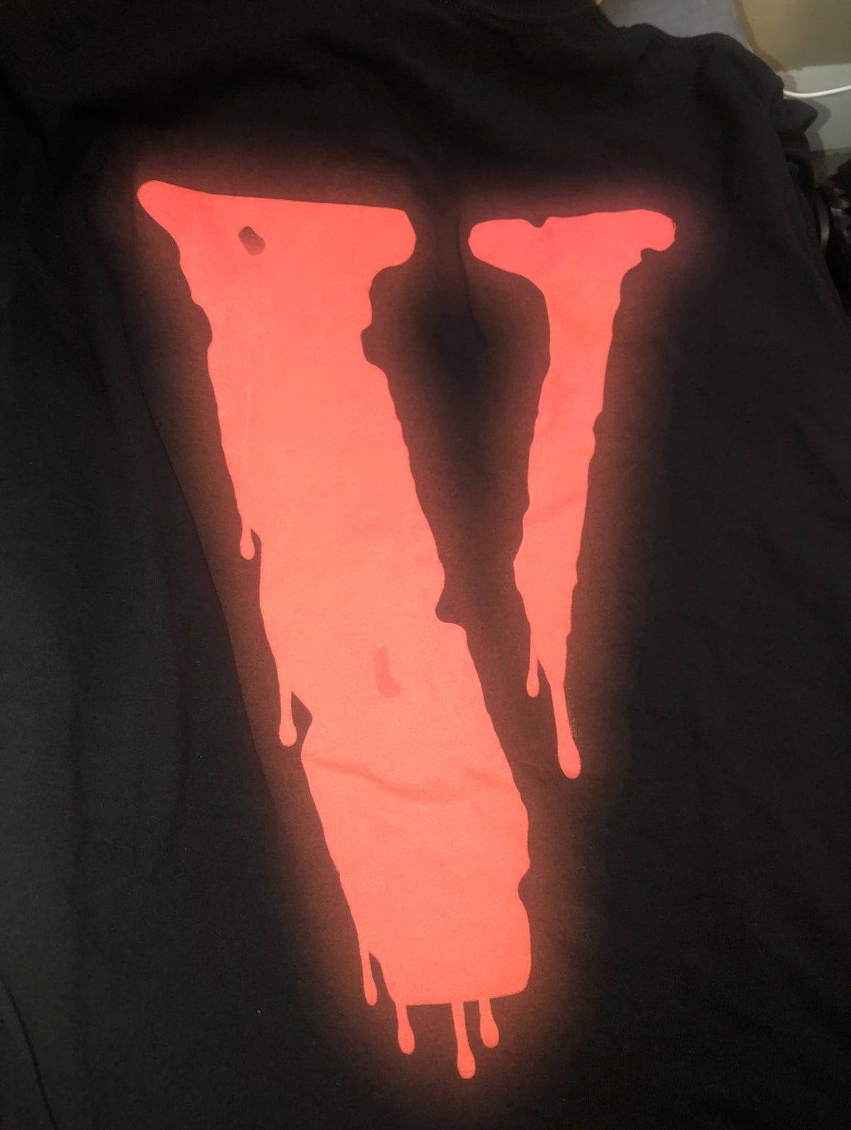 Vlone 桌布 壁紙 — 一件黑色T恤在深色背景上展示了一個發光的橙色滴落「V」標誌。