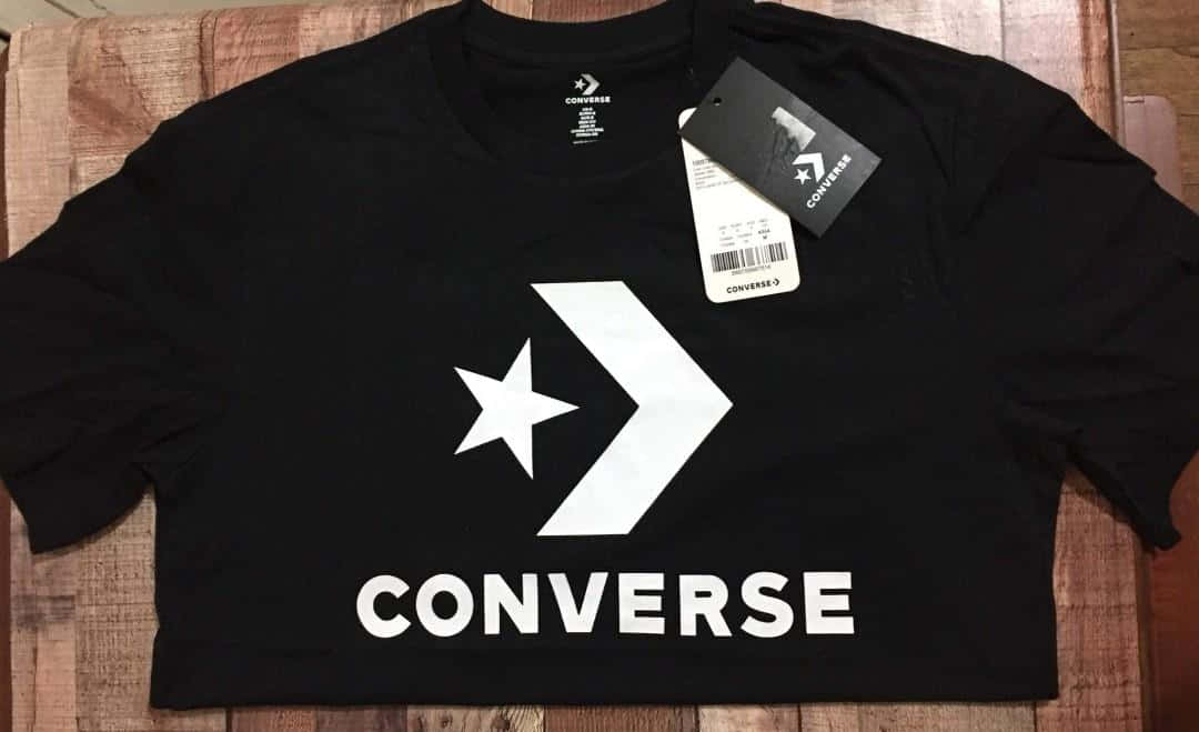 Converse 桌布 壁紙 — 一件黑色短版Converse T恤，帶有白色標誌，平放在木質表面上，標籤仍附著。