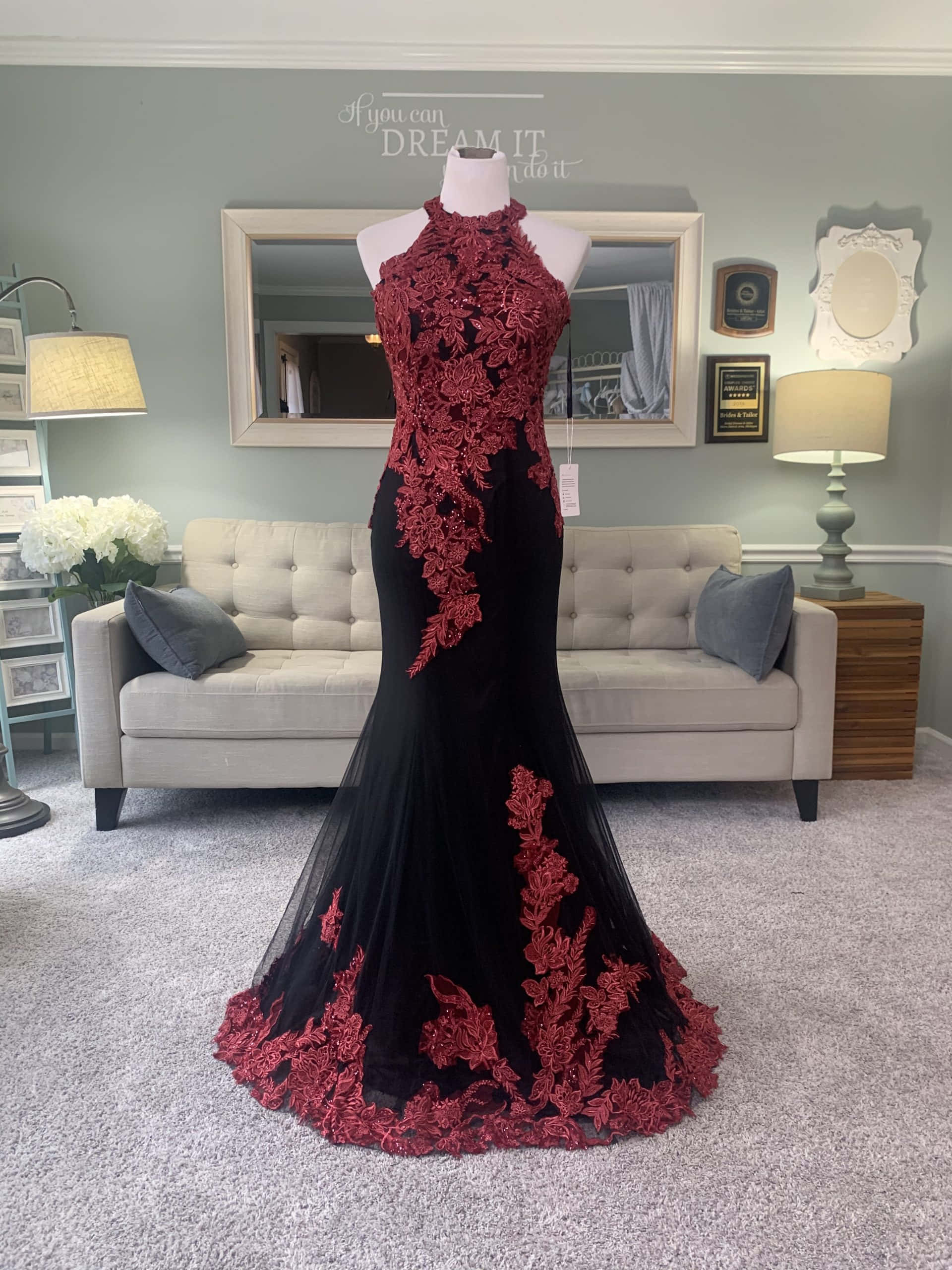 Red Wedding 桌布 壁紙 — 一件黑色美人魚禮服，帶有紅色花卉蕾絲細節，展示在柔和光線的客廳中的人體模型上。