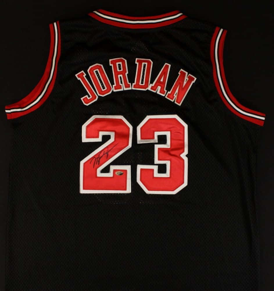 桌布 壁紙 — 一件黑色芝加哥公牛隊球衣，帶有紅白飾邊，展示 'JORDAN' 及號碼 '23'，以粗體紅色配白色輪廓，號碼下方有簽名。