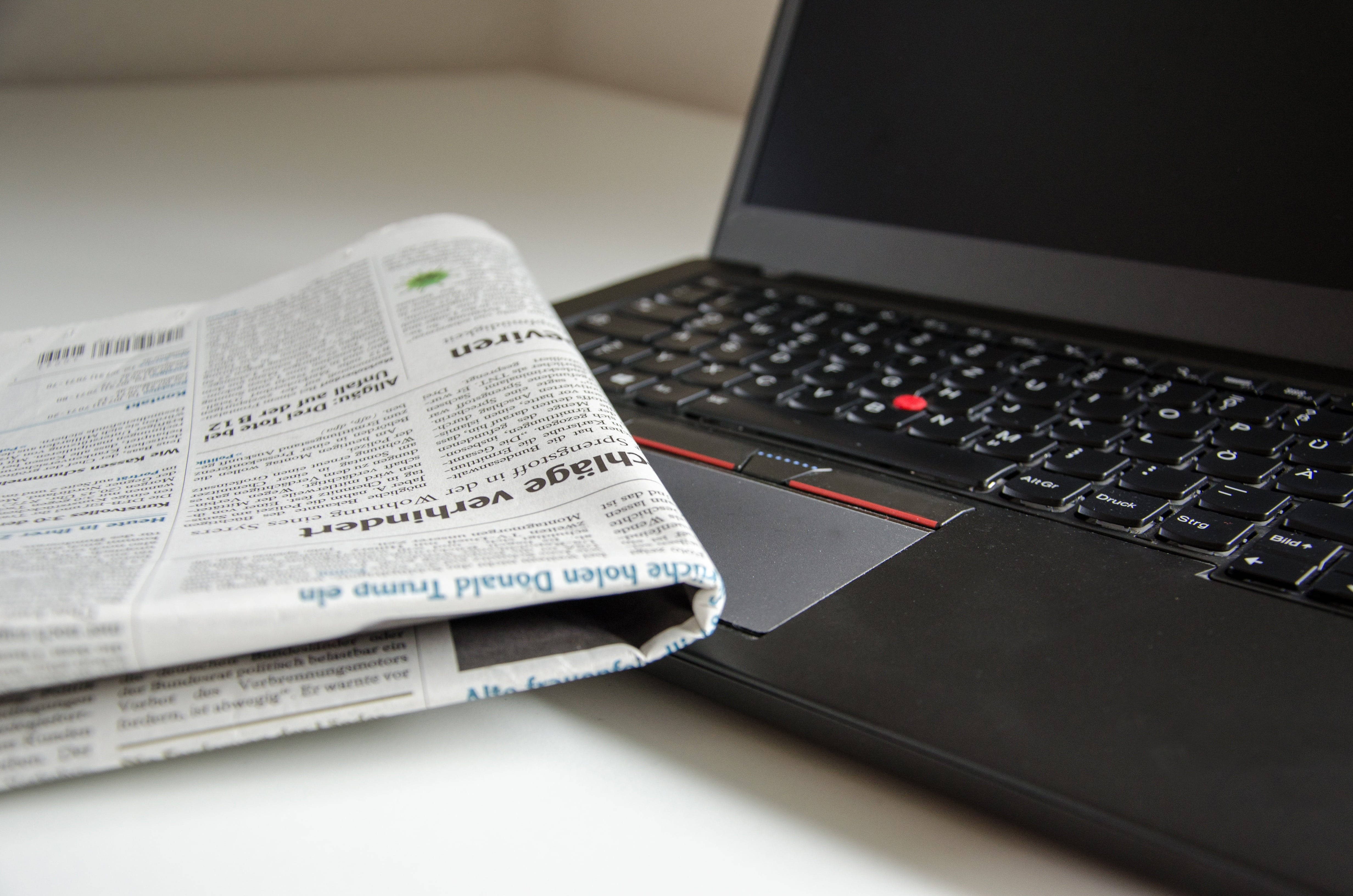 Newspaper 桌布 壁紙 — 一份折疊的報紙放在現代工作空間的白色桌子上，旁邊是一部黑色筆記型電腦。