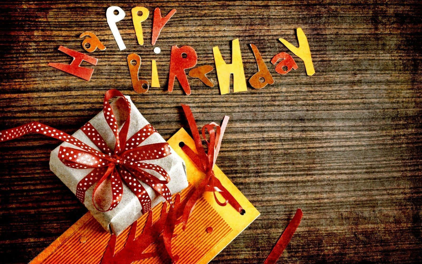 生日快樂 桌布 壁紙 — 一份用銀紙包裹、帶有紅色圓點蝴蝶結的節日生日禮物，旁邊放著色彩繽紛的剪字，拼出 'Happy Birthday'，置於質樸的木質表面上。