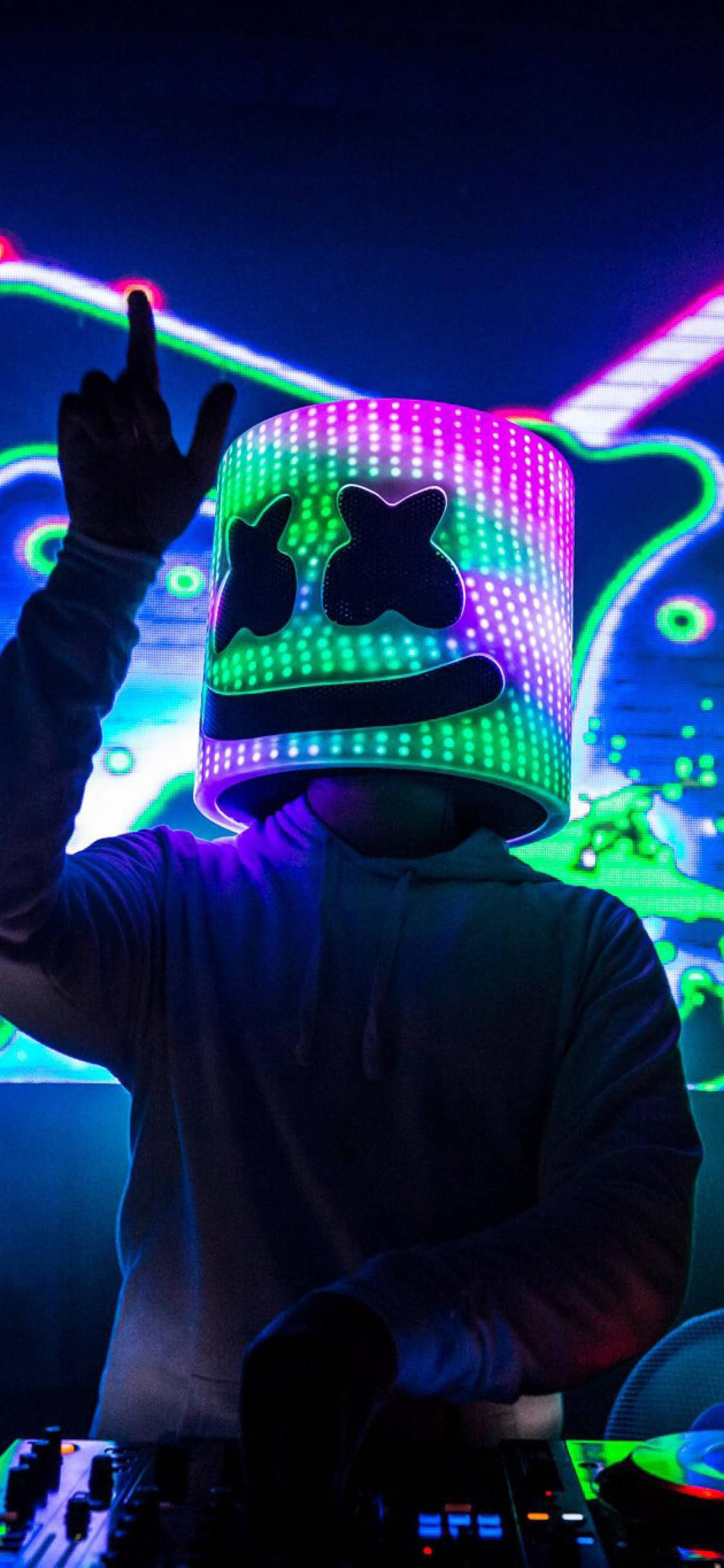 marshmello iPhone 桌布 壁紙 — 一位DJ戴著發光的LED頭盔，X形眼睛和微笑，在充滿彩色光軌的霓虹燈俱樂部表演。