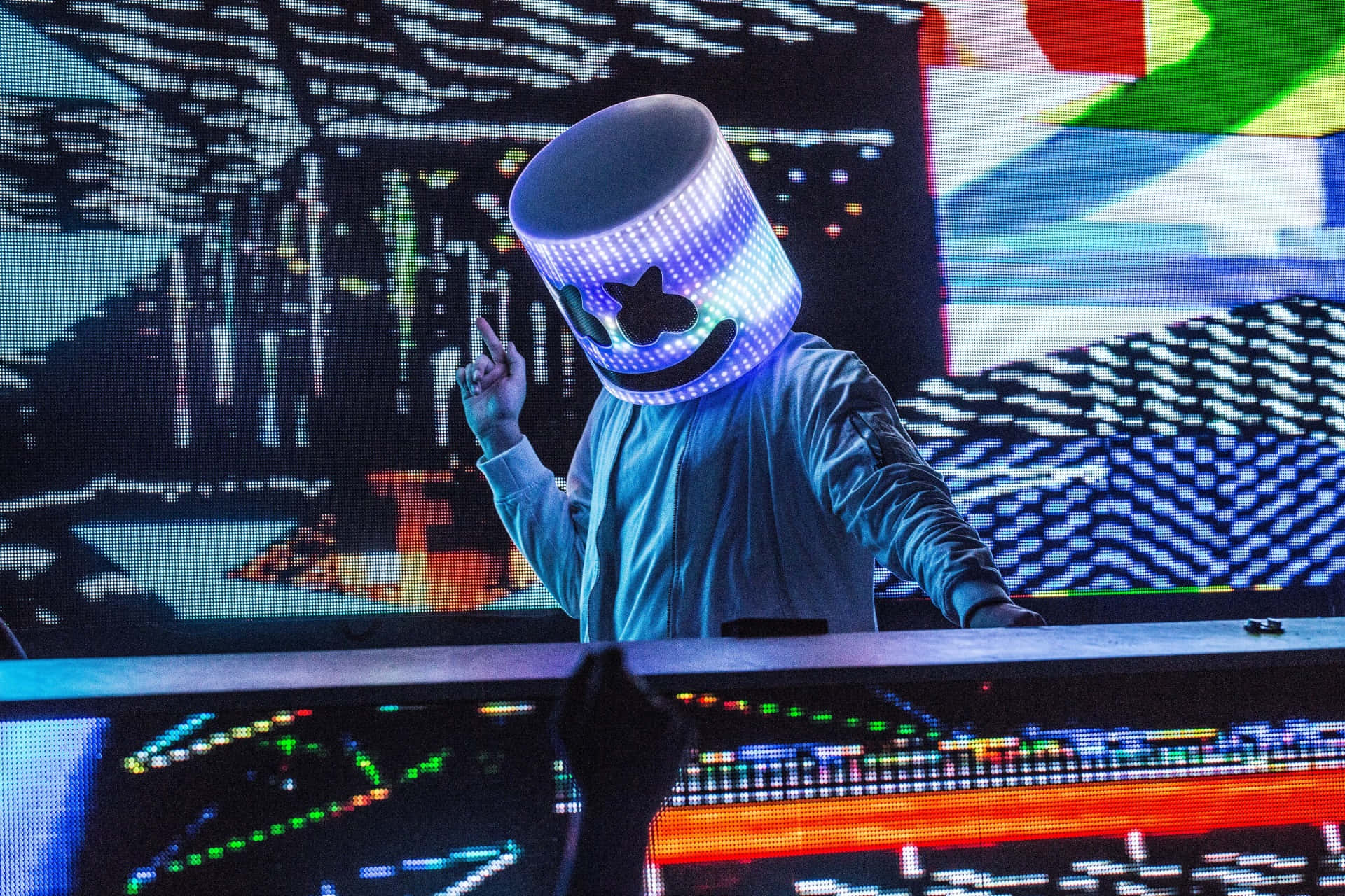Marshmello 動態圖 桌布 壁紙 — 一位DJ戴著發光的藍色LED棉花糖面具，在充滿活力的電子音樂節上表演，身後是色彩繽紛的數位螢幕。