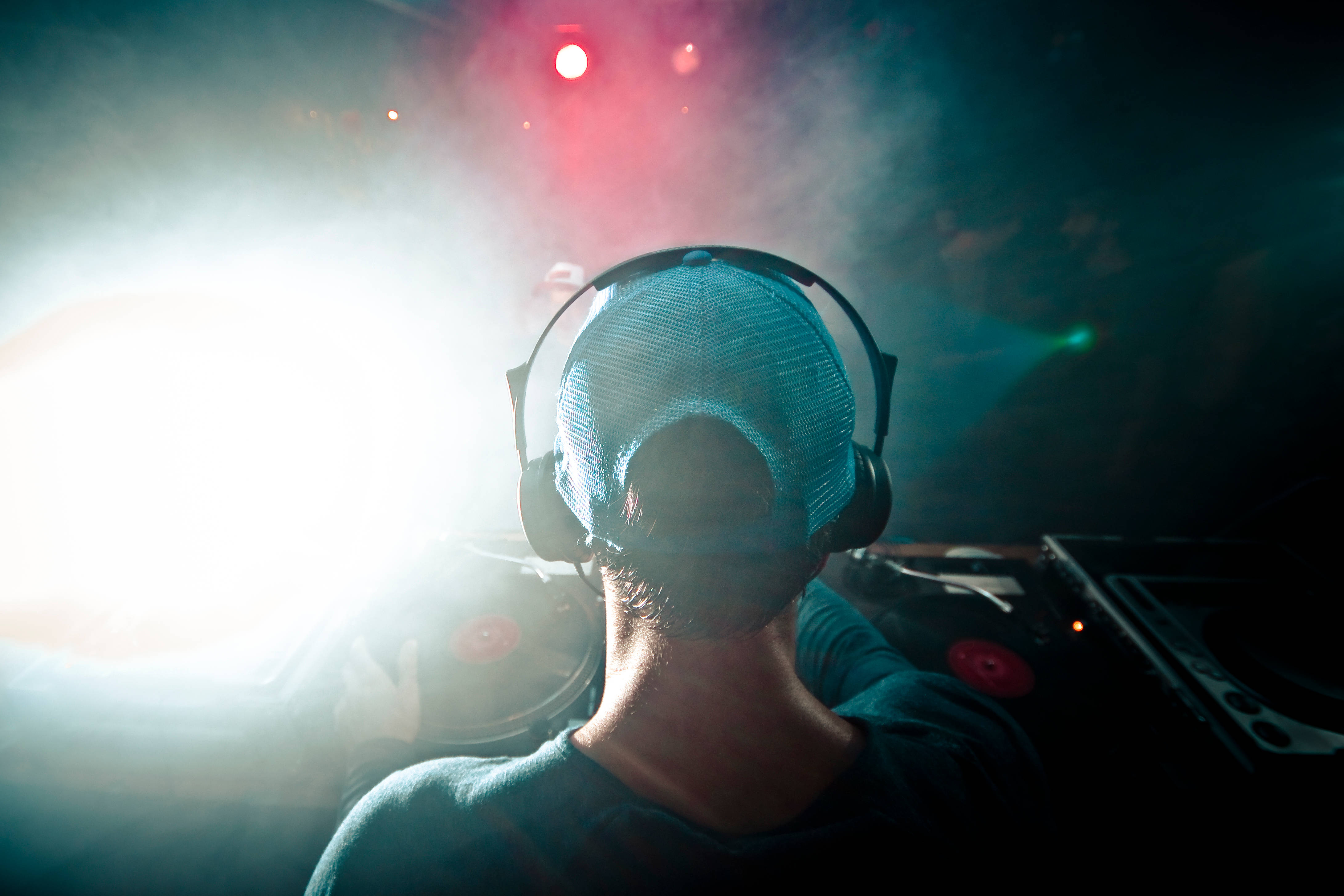 DJ 桌布 壁紙 — 一位DJ戴著耳機和網帽，在演唱會上以明亮的舞台燈光和煙霧為背景形成剪影。