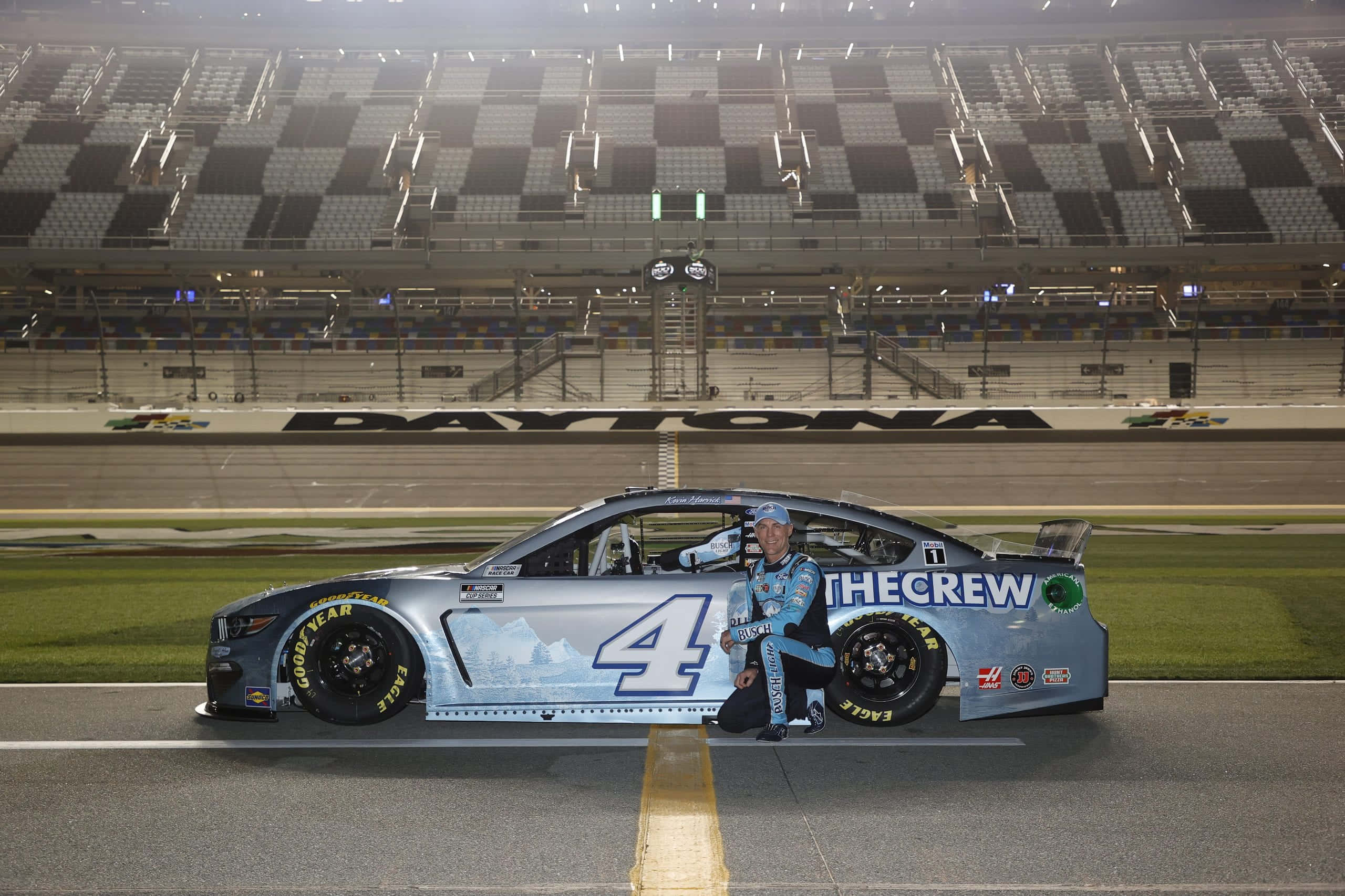 nascar 桌布 壁紙 — 一位NASCAR車手在體育場燈光下，跪在代托納賽道上他的藍色4號賽車旁。