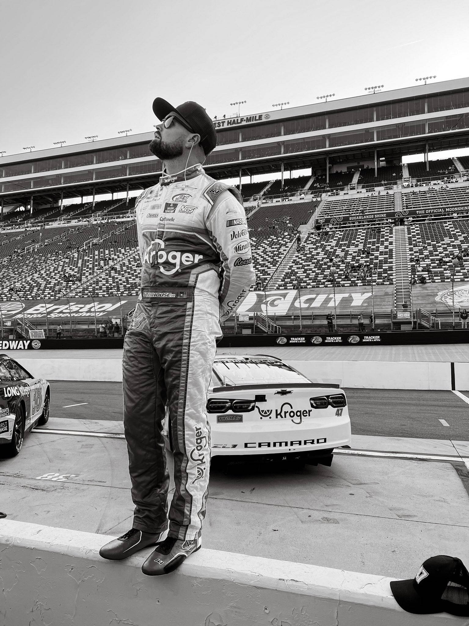 Athlete 桌布 壁紙 — 一位NASCAR車手身穿全套賽車裝備，在賽道上沉思地站在他的雪佛蘭Camaro賽車旁邊。