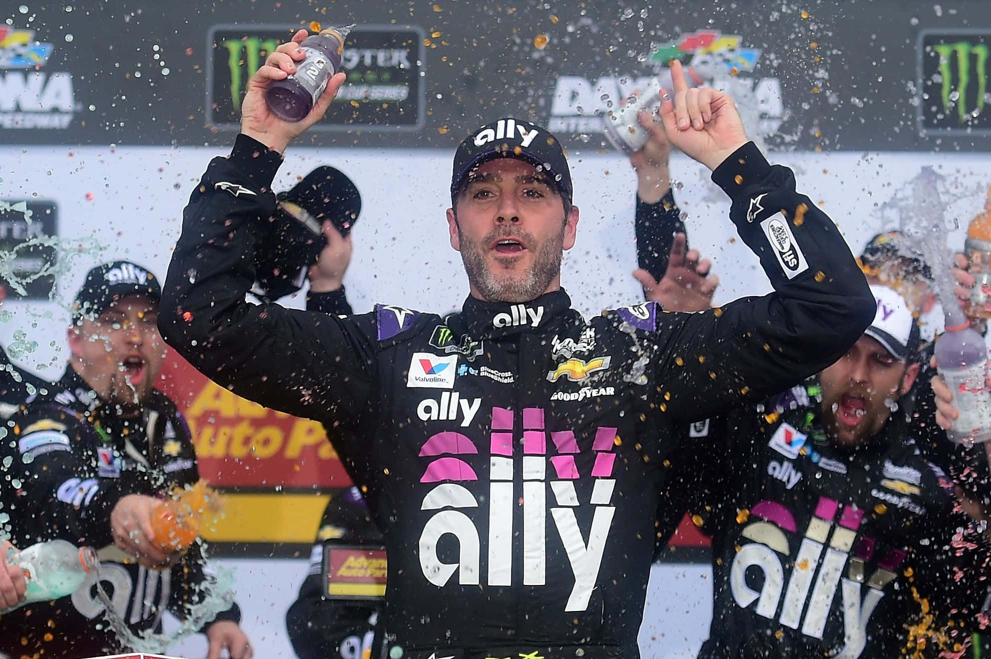 Jimmie Johnson 桌布 壁紙 — 一位NASCAR車手身穿同盟賽車服在頒獎台上慶祝勝利，周圍噴灑著五彩紙屑和香檳。