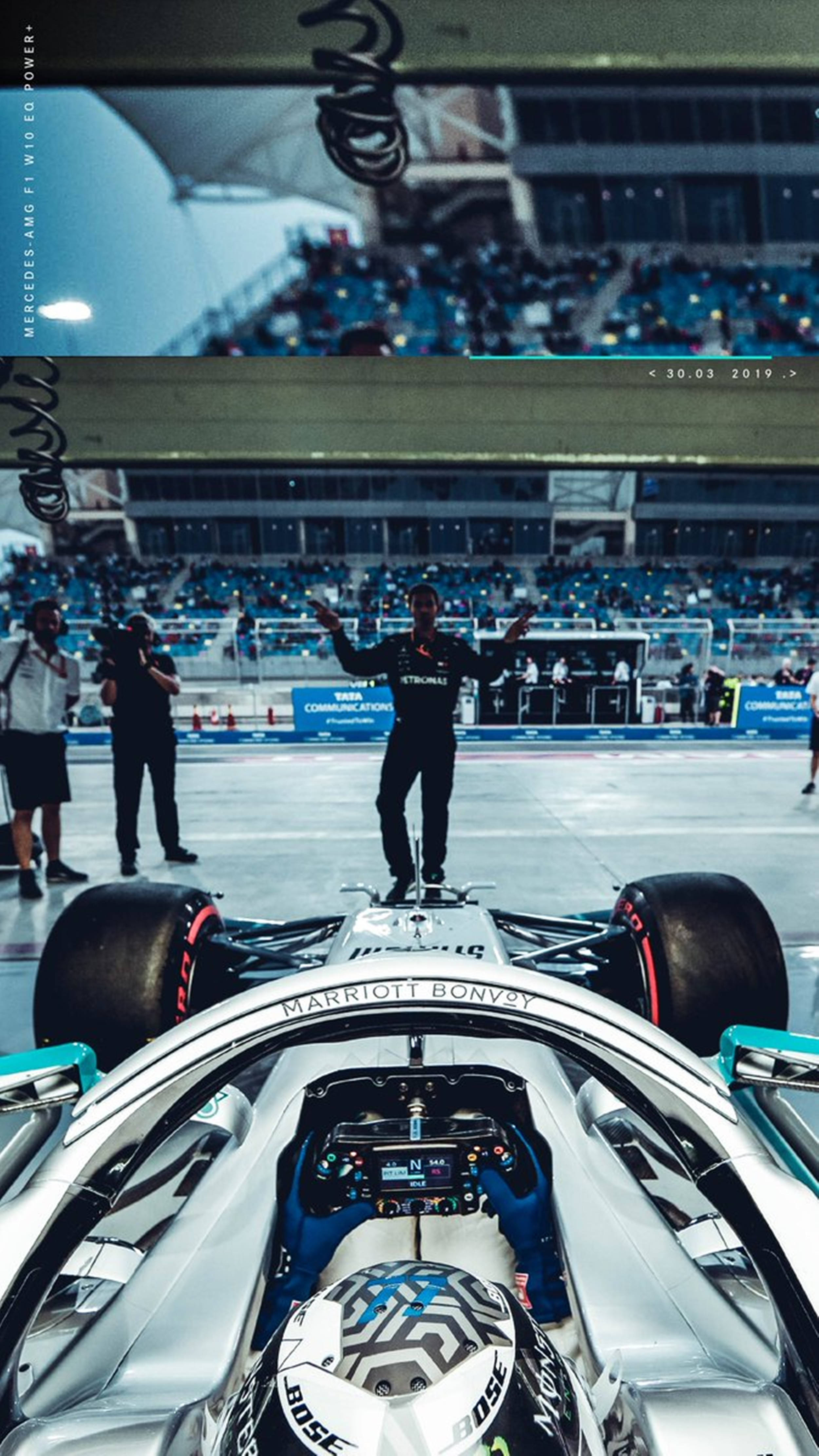 F1 桌布 壁紙 — 一位一級方程式車手站在他銀色的賓士賽車上，在一個擠滿車迷的體育館內慶祝勝利。