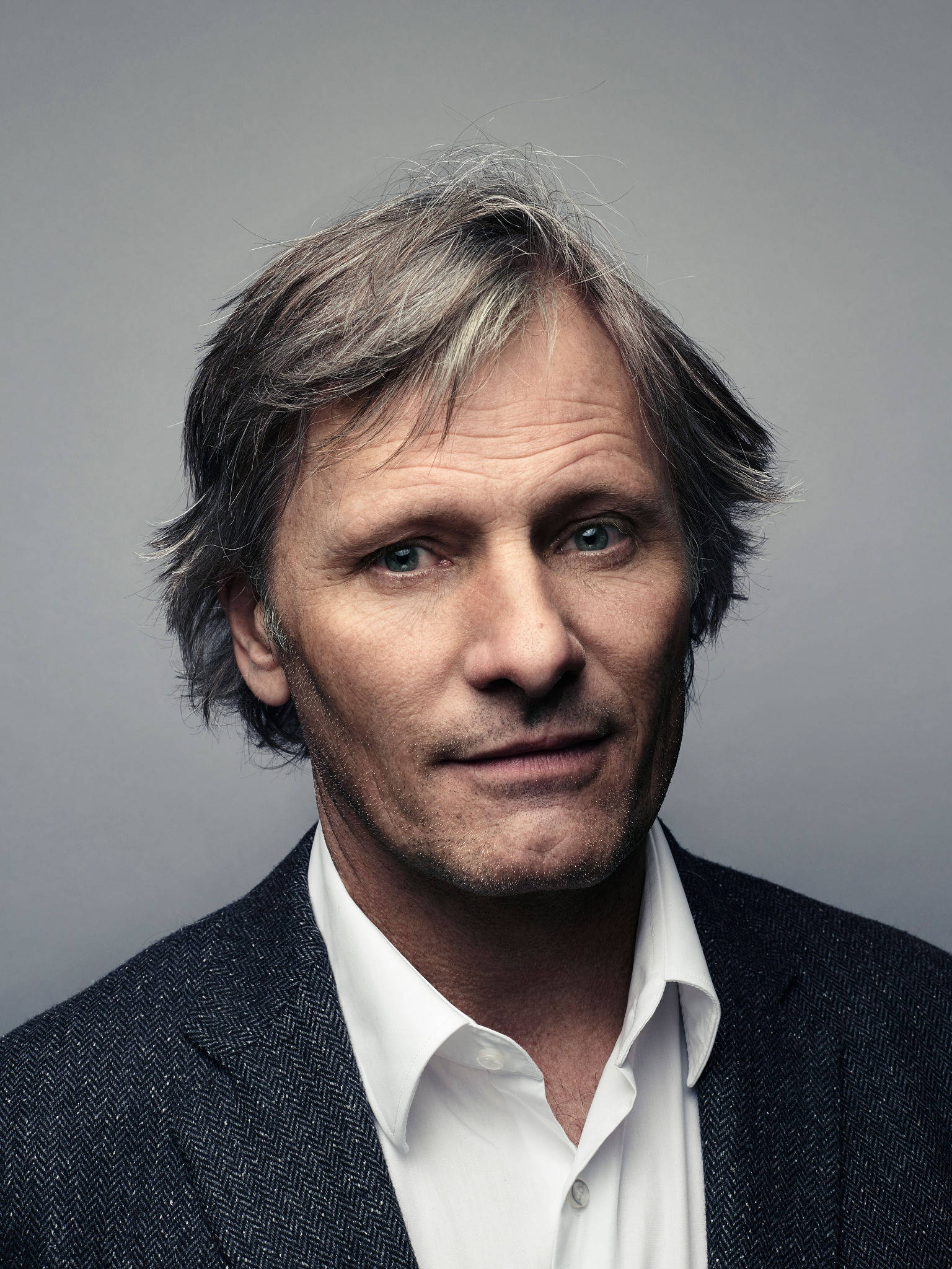 actor 桌布 壁紙 — 一位中年男士的特寫肖像，頭髮花白，藍色眼睛深邃，身穿深色質感西裝外套，內搭白襯衫，背景為中性灰色。