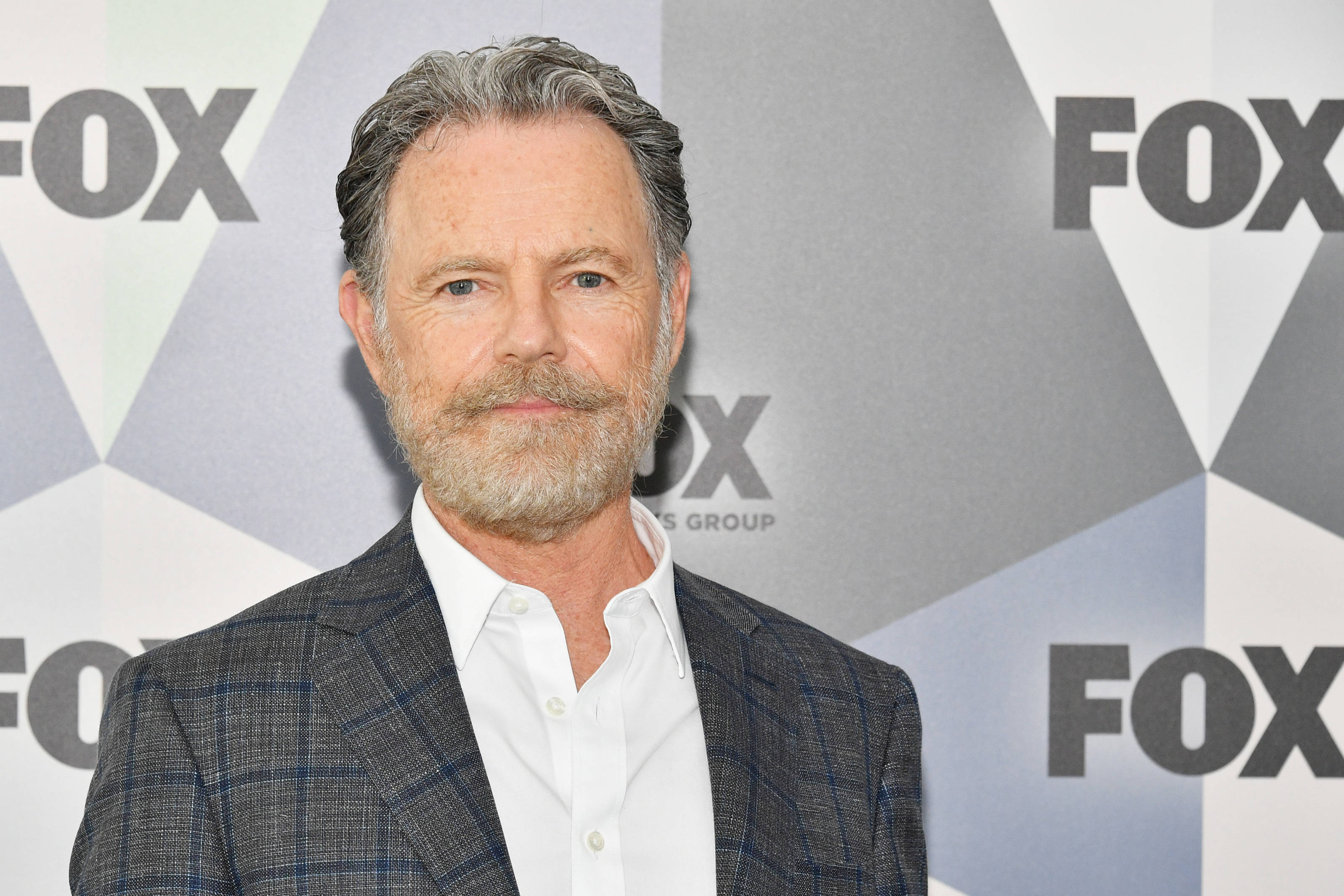 actor 桌布 壁紙 — 一位中年男子，灰髮鬍鬚，身穿格紋西裝外套，內搭白襯衫，背景為幾何FOX圖案。