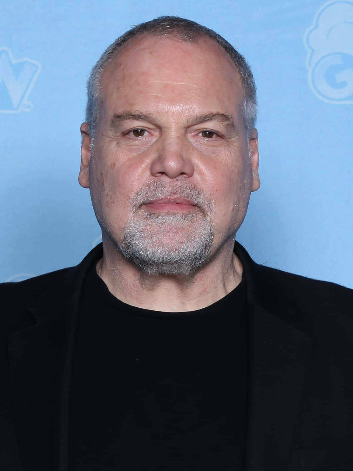 Vincent D'onofrio 桌布 壁紙 — 一位中年男子的近距離肖像，他有灰白頭髮和鬍鬚，穿著黑色西裝，背景是淺藍色。