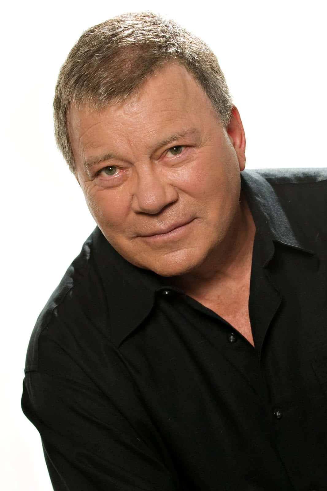 william shatner 桌布 壁紙 — 一位中年男子的近距離肖像，短灰白頭髮，穿著黑色襯衫，背景是純白色。