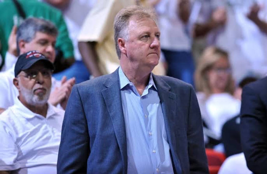 larry bird 桌布 壁紙 — 一位中年男子身穿藍色西裝外套和條紋襯衫，在擁擠的室內體育賽事中表情嚴肅地站著。