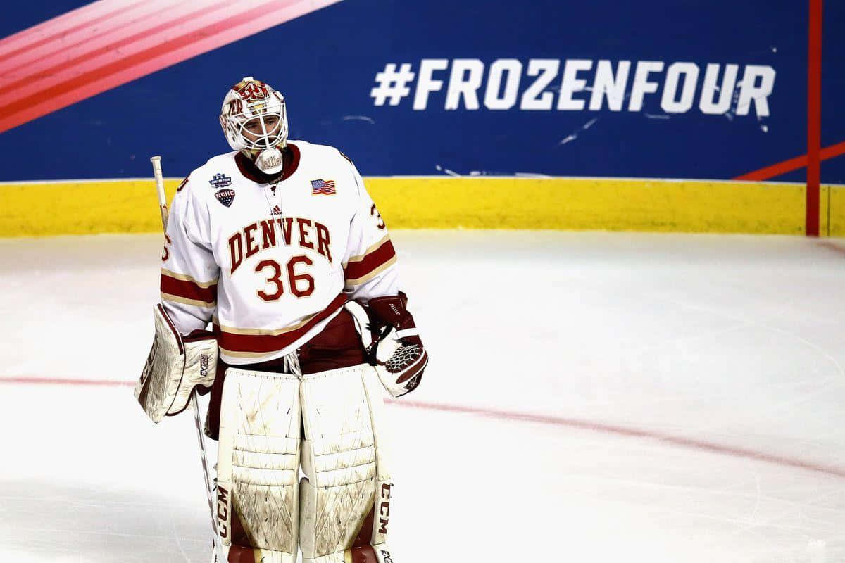 hockey 桌布 壁紙 — 一位丹佛冰球守門員身穿白色和栗色裝備，在 '#FROZENFOUR' 橫幅下莊嚴地站在冰上。