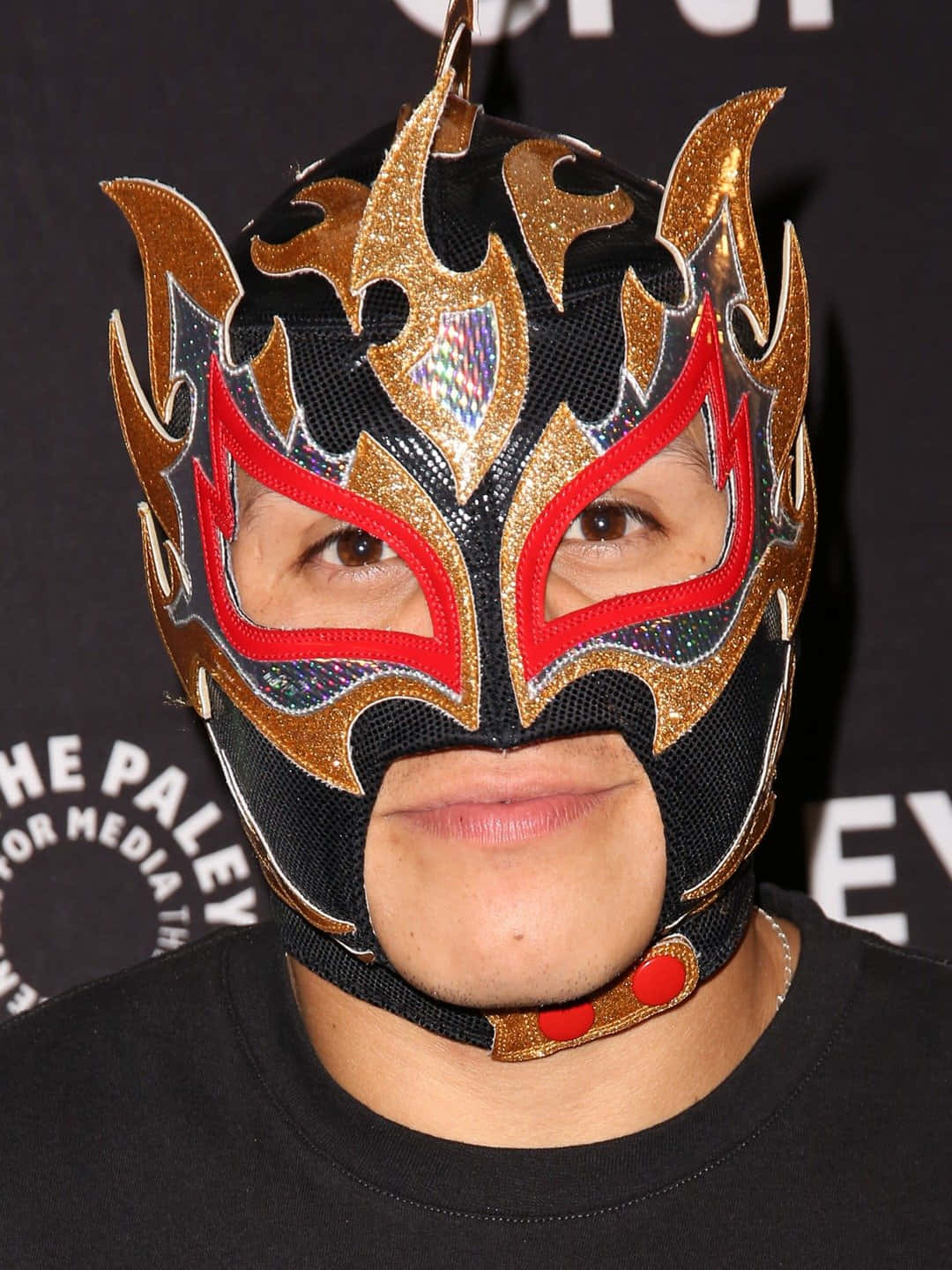 Mask 桌布 壁紙 — 一位人士在媒體活動中戴著閃亮的黑金紅色自由摔角面具，帶有火焰圖案。