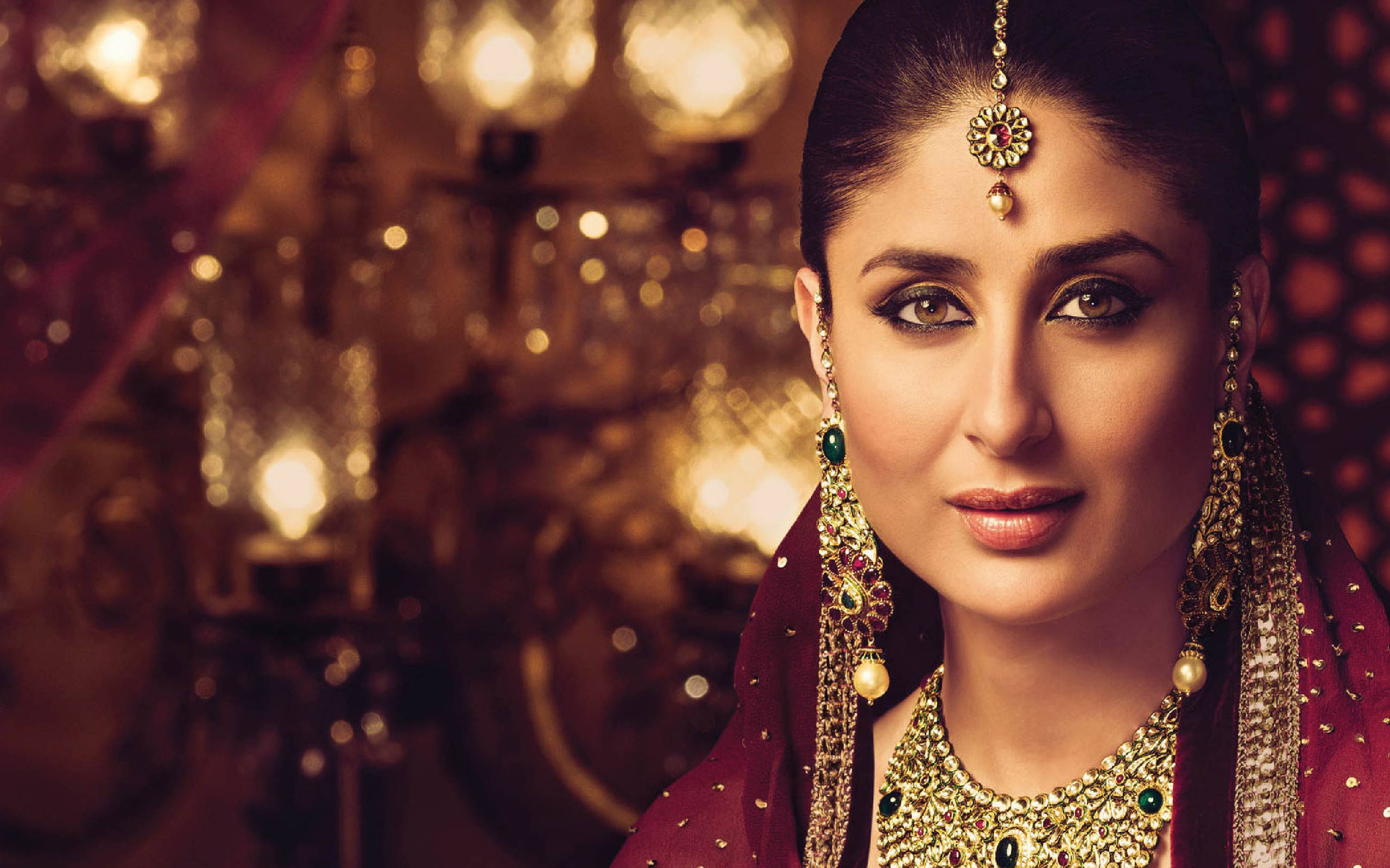 Kareena 桌布 壁紙 — 一位佩戴華麗傳統珠寶、身穿栗色服飾的女性，在溫暖燈光下、掛著燈籠的散景背景中溫柔凝視。