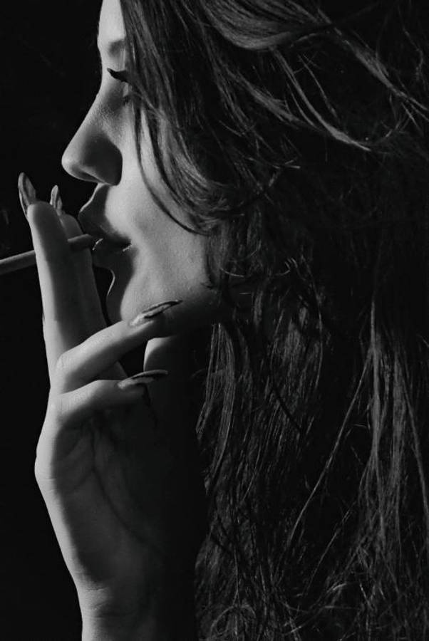 抽菸 桌布 壁紙 — 一位側面輪廓的女性在黑暗背景下抽煙，帶有戲劇性的明暗對比燈光。