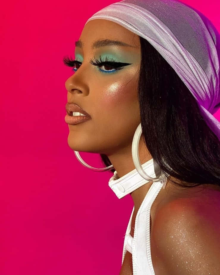 Doja Cat 桌布 壁紙 — 一位側面輪廓的女性戴著銀色頭巾，在充滿活力的粉紅色背景上畫著大膽的藍綠色眼妝。