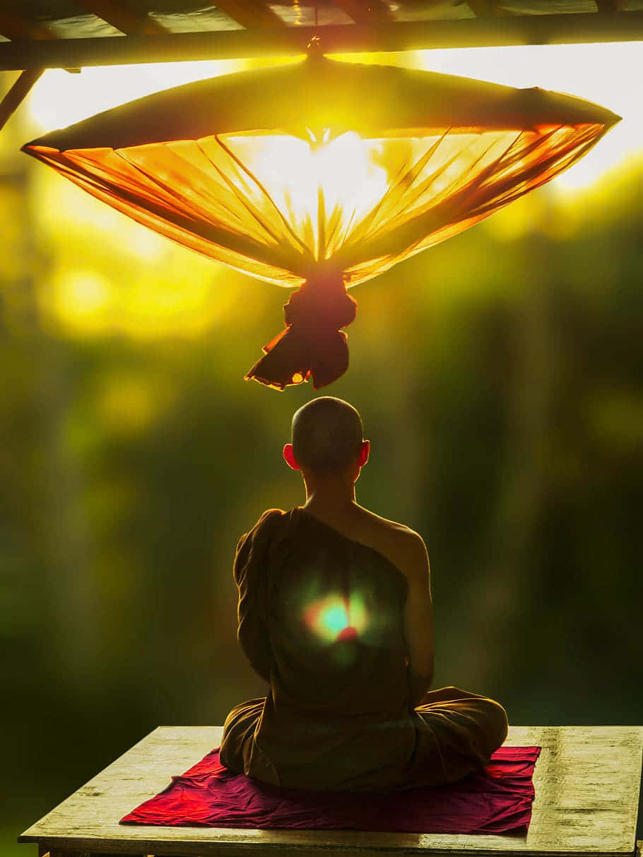 Spiritual Meditation 桌布 壁紙 — 一位僧侶在發光的金色雨傘下冥想坐著，陽光穿過布料形成燦爛的光環效果。