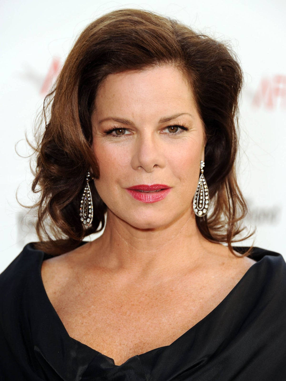 Celebrity 桌布 壁紙 — 一位優雅女性，波浪棕色長髮，佩戴閃爍吊燈耳環，身穿黑色連衣裙，以白色背景為襯。