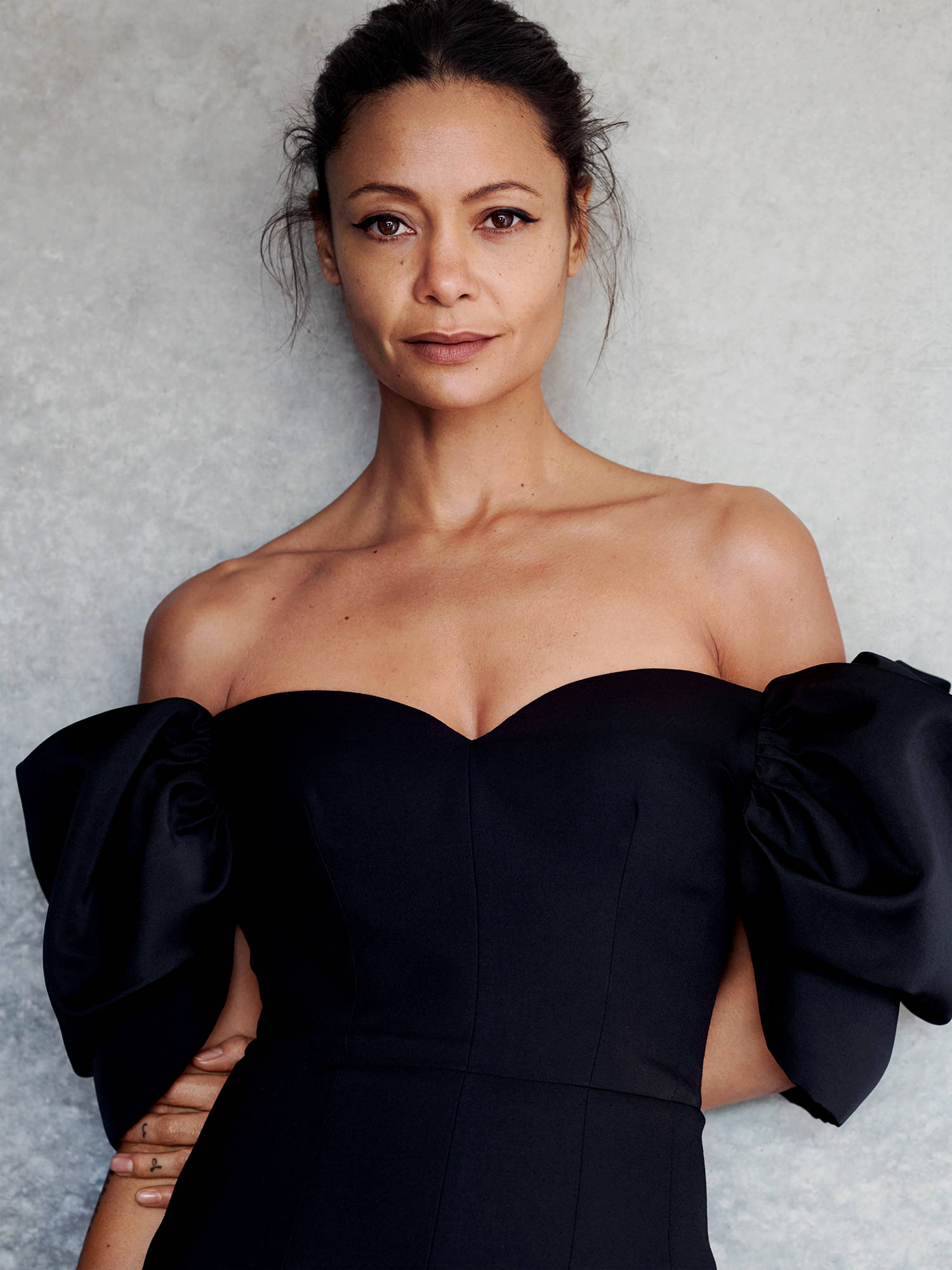Actress HD 桌布 壁紙 — 一位優雅女性身穿黑色露肩連衣裙，袖管寬大，站在有紋理的灰色背景前。