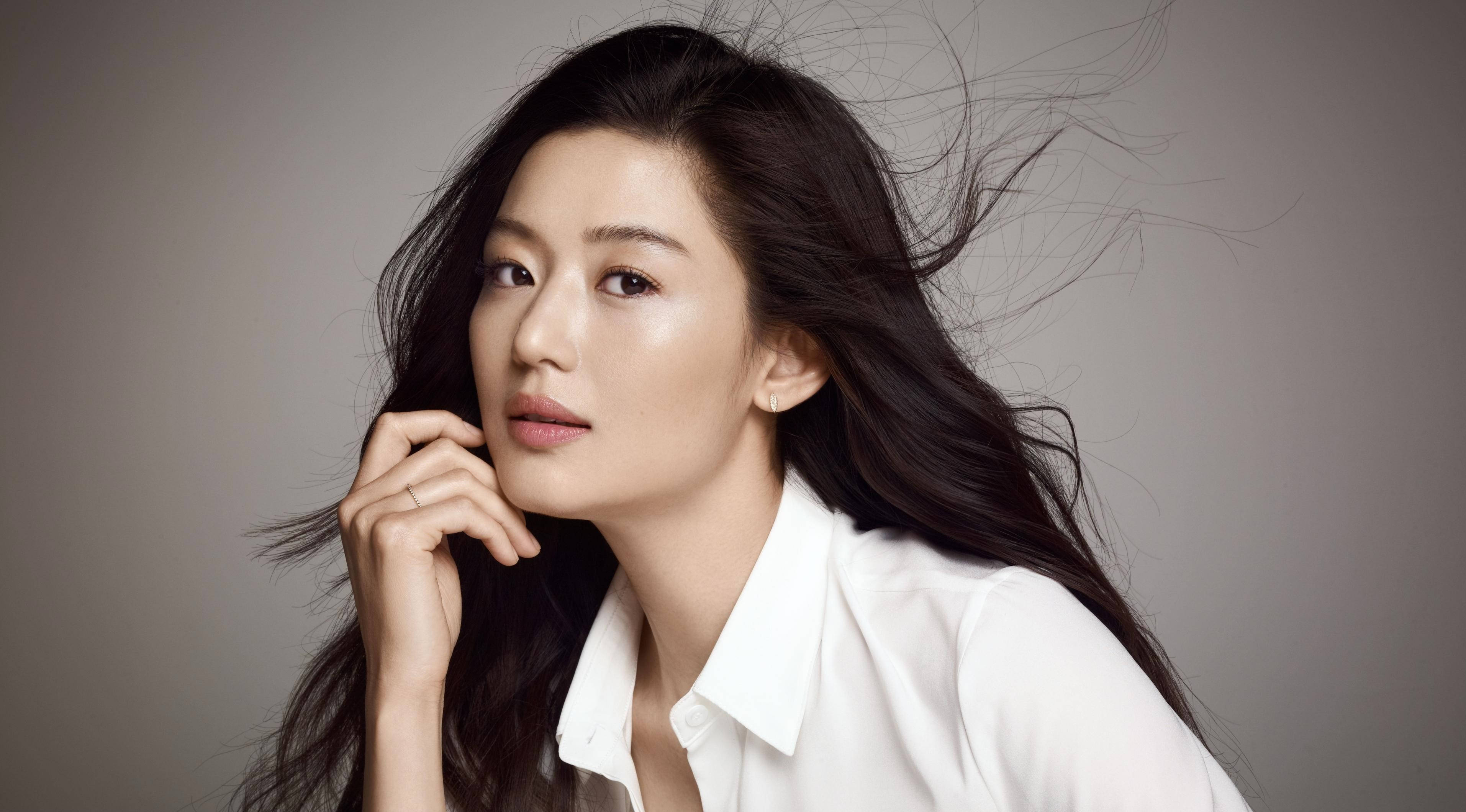 Jun Ji Hyun 桌布 壁紙 — 一位優雅的女人，擁有飄逸的深色頭髮和白色襯衫，在柔和的灰色背景下若有所思地凝視。