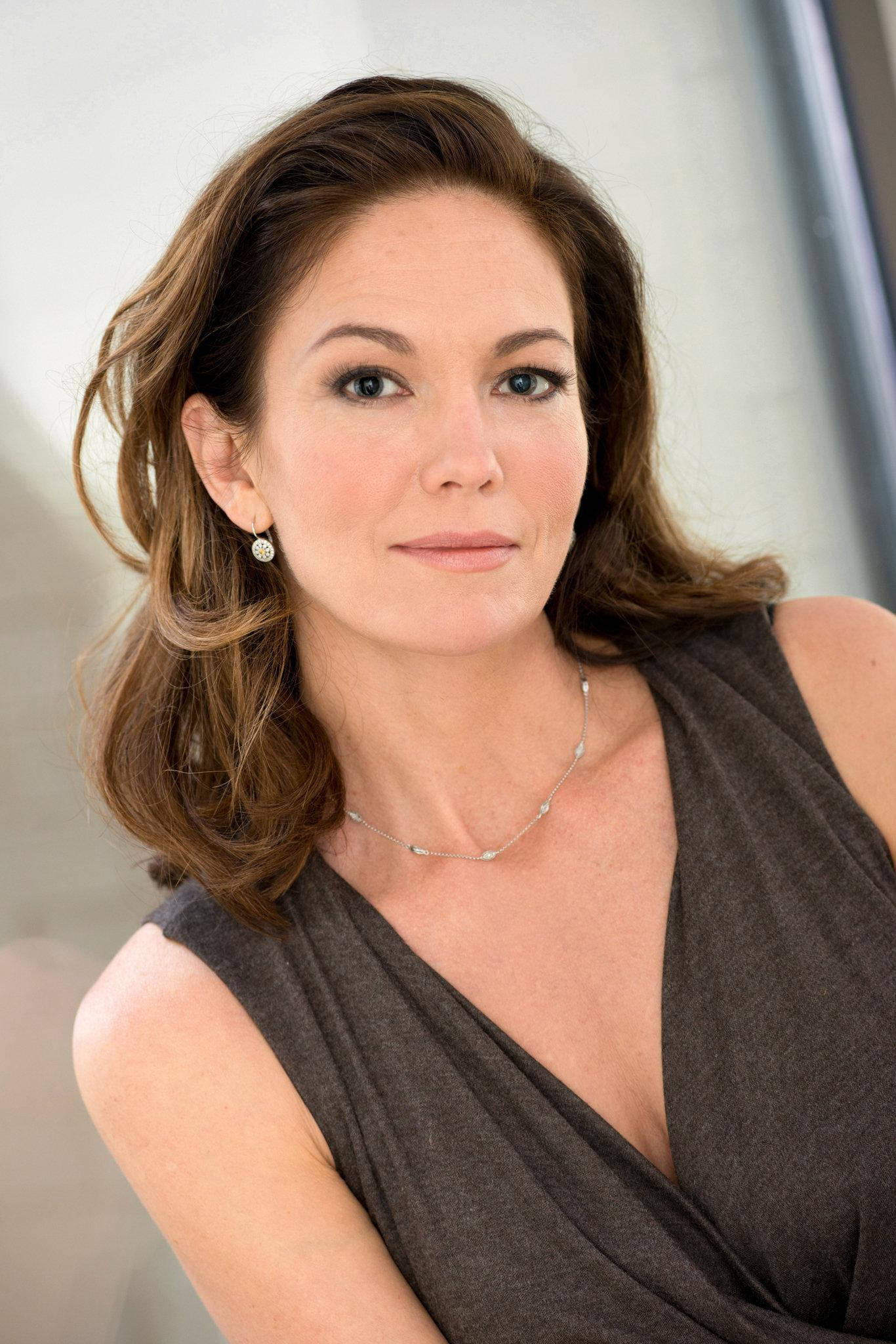 Diane Lane 桌布 壁紙 — 一位優雅的女人，波浪般的棕色頭髮和精緻的珠寶，在柔和的工作室燈光下平靜地凝視著相機。