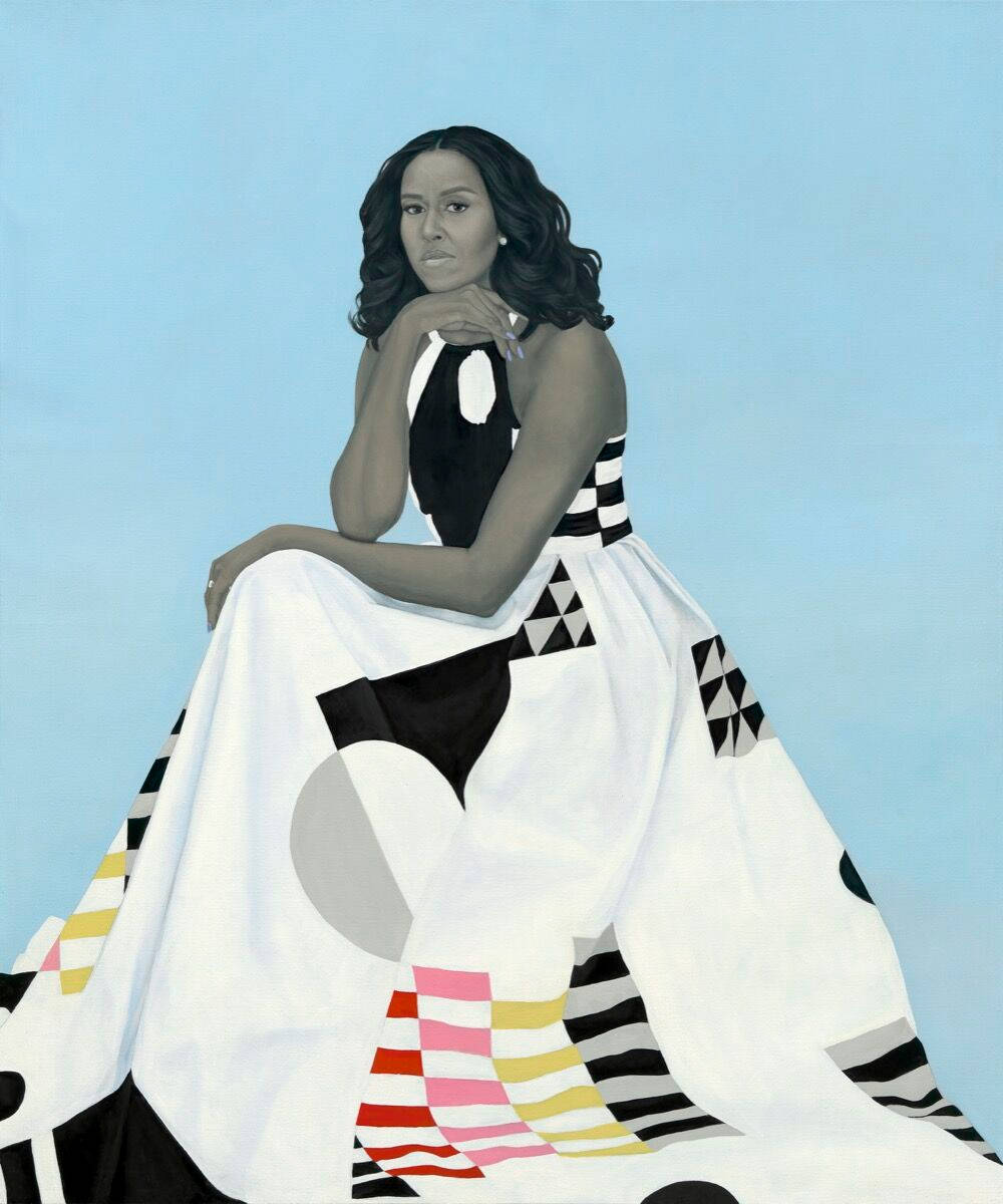 Michelle 桌布 壁紙 — 一位優雅的女士身穿大膽的幾何圖案長裙，坐在柔和的藍色背景前，表情平靜而從容。