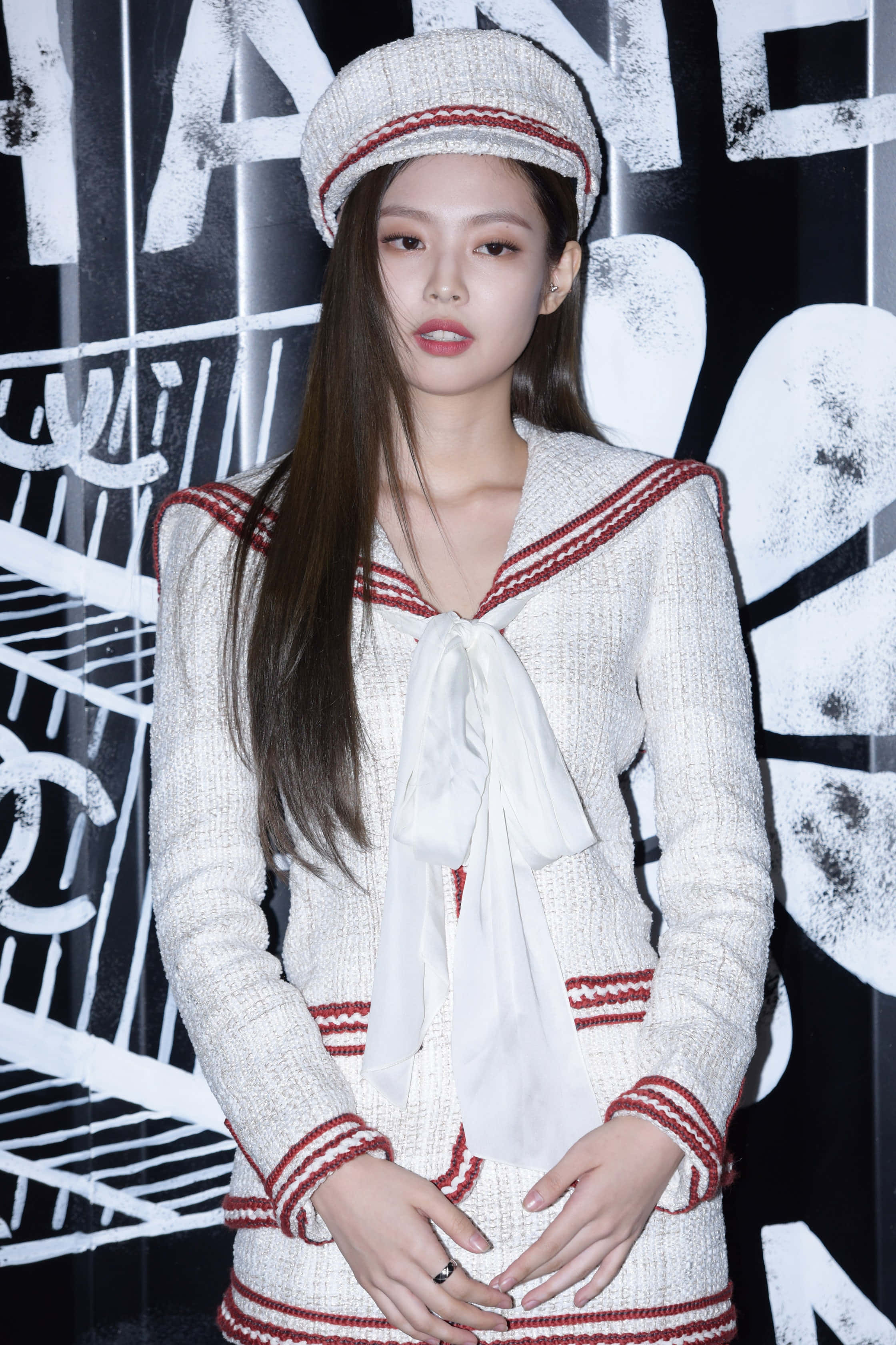 BLACKPINK 桌布 壁紙 — 一位優雅的女士身穿白色粗花呢水手服，配有紅色飾邊和相配的帽子，站在大膽的黑白 Chanel 標誌背景前。