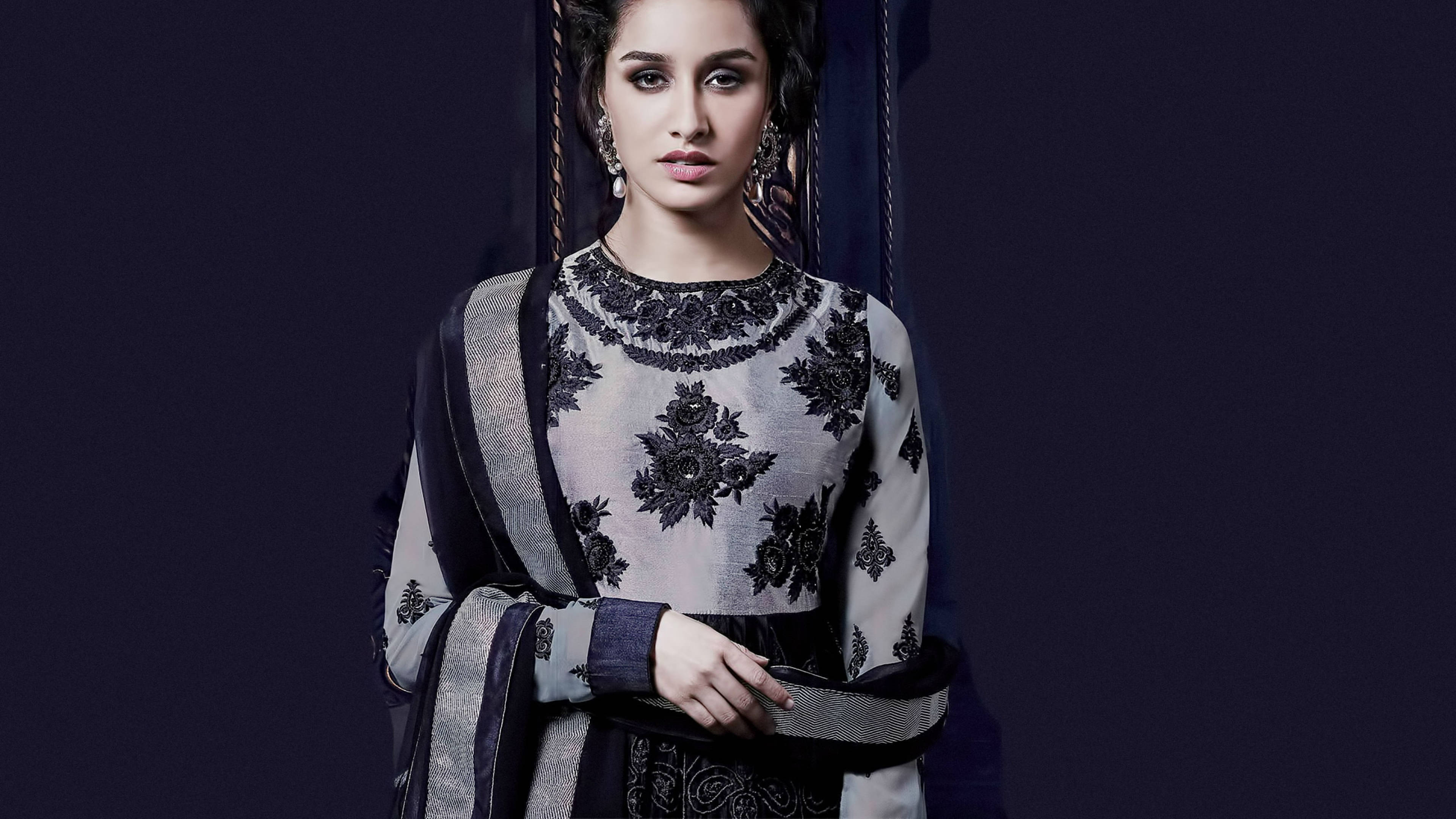 Shraddha Kapoor 桌布 壁紙 — 一位優雅的女士身穿華麗的黑色和銀色刺繡服裝，站在深紫色背景前，燈光效果戲劇化。