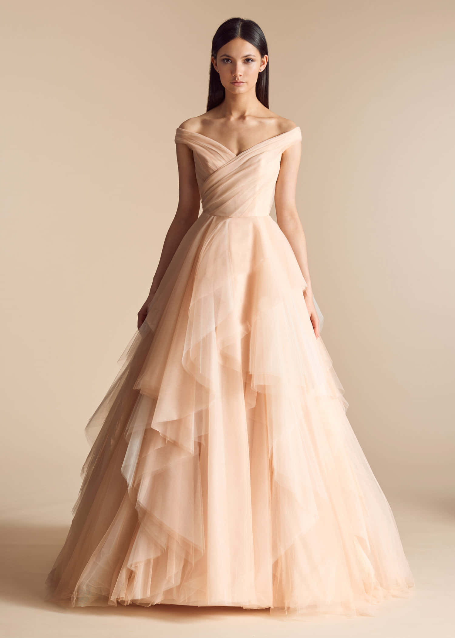 Wedding Gown 桌布 壁紙 — 一位優雅的女士身穿飄逸的蜜桃色薄紗長裙，搭配垂墜式上身，站在柔和的米色攝影棚背景前。