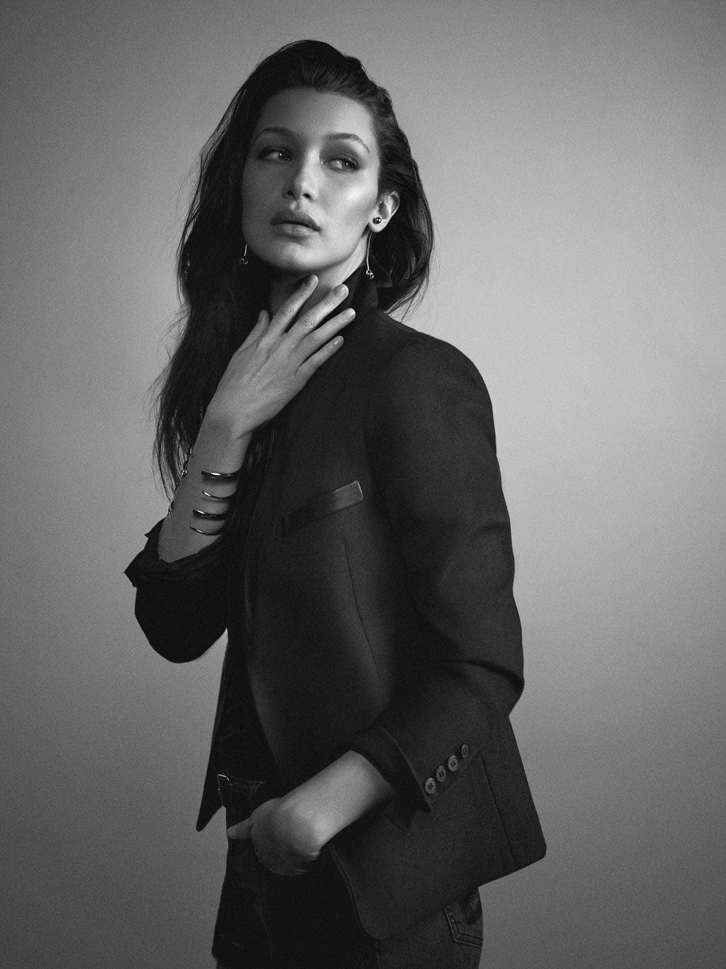 Bella Hadid 桌布 壁紙 — 一位優雅的女士身穿黑色西裝外套，在灰色背景前擺姿勢，一隻手靠近頸部。