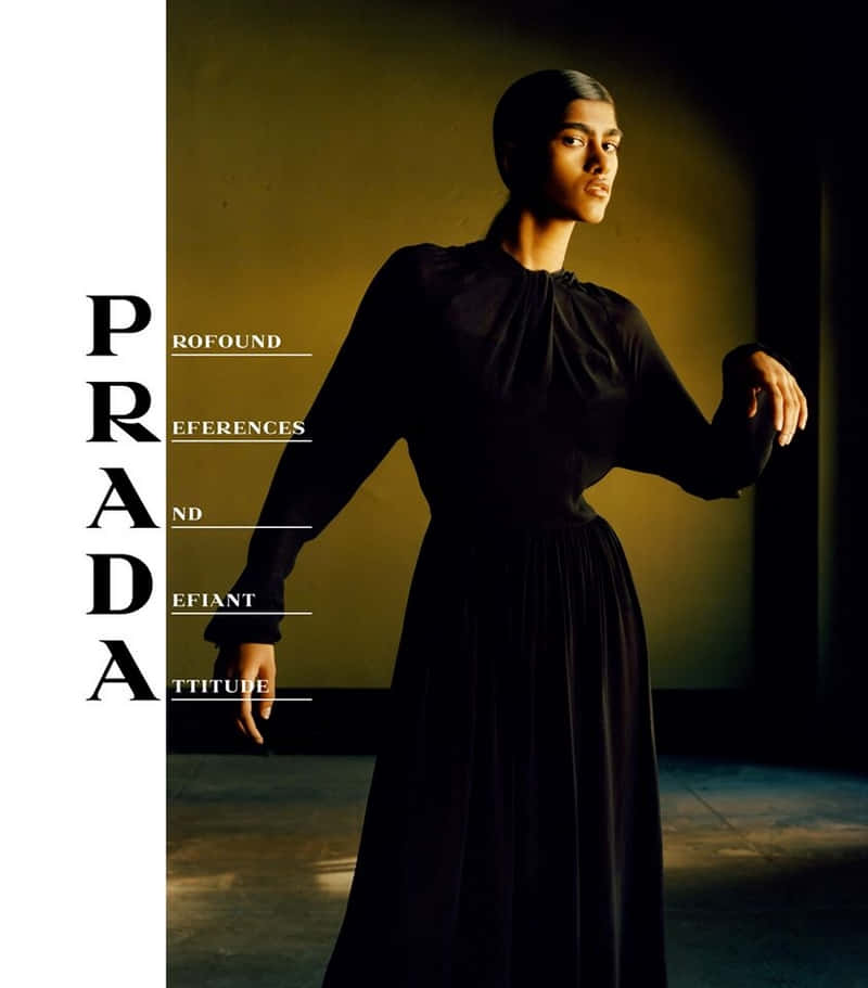 Prada 桌布 壁紙 — 一位優雅的模特兒穿著黑色長裙，在極簡工作室背景下，站在戲劇性的金色光線中，並帶有醒目的Prada字體。