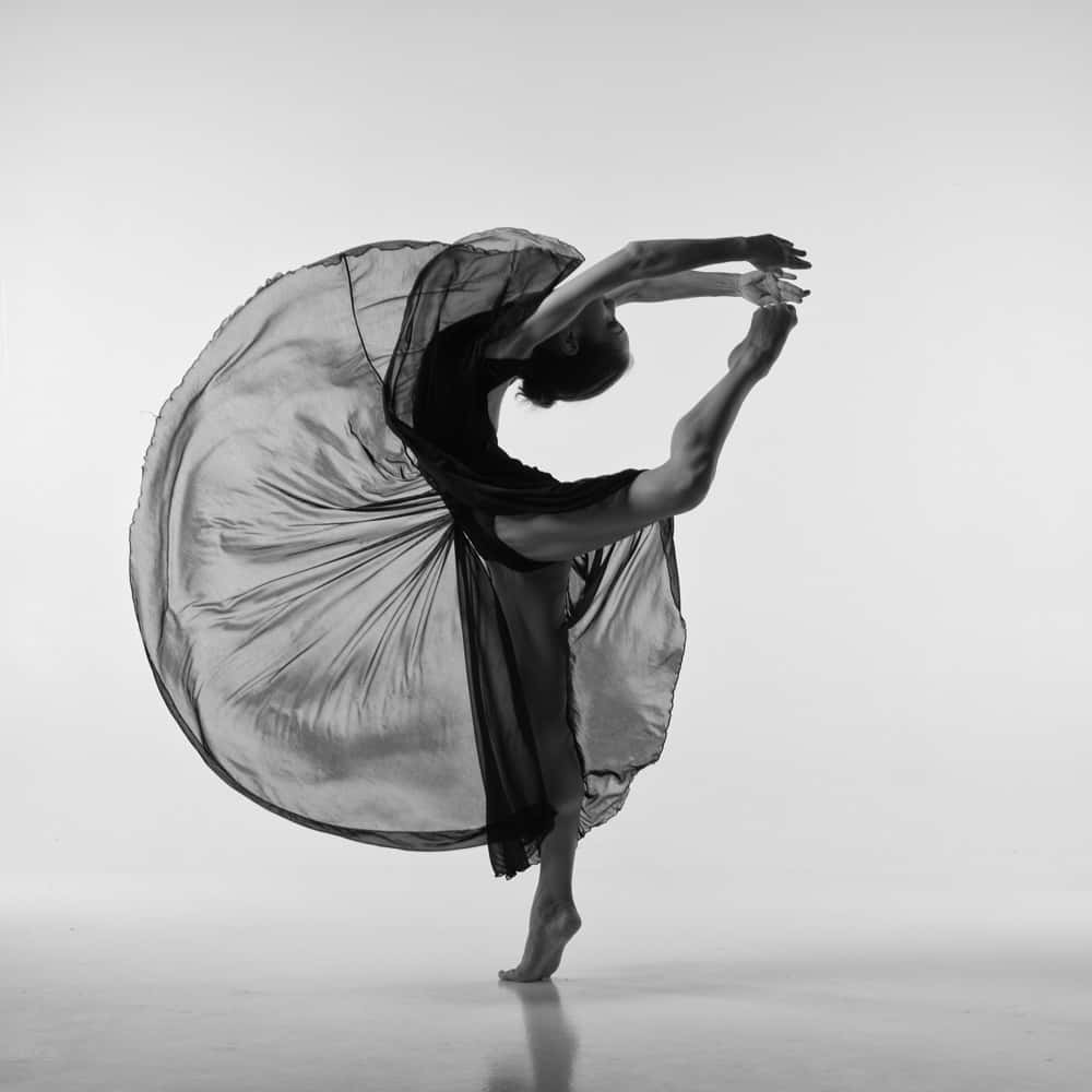 dancer 桌布 壁紙 — 一位優雅的舞者身穿飄逸的黑色布料，在純白的工作室背景下以單色旋轉。
