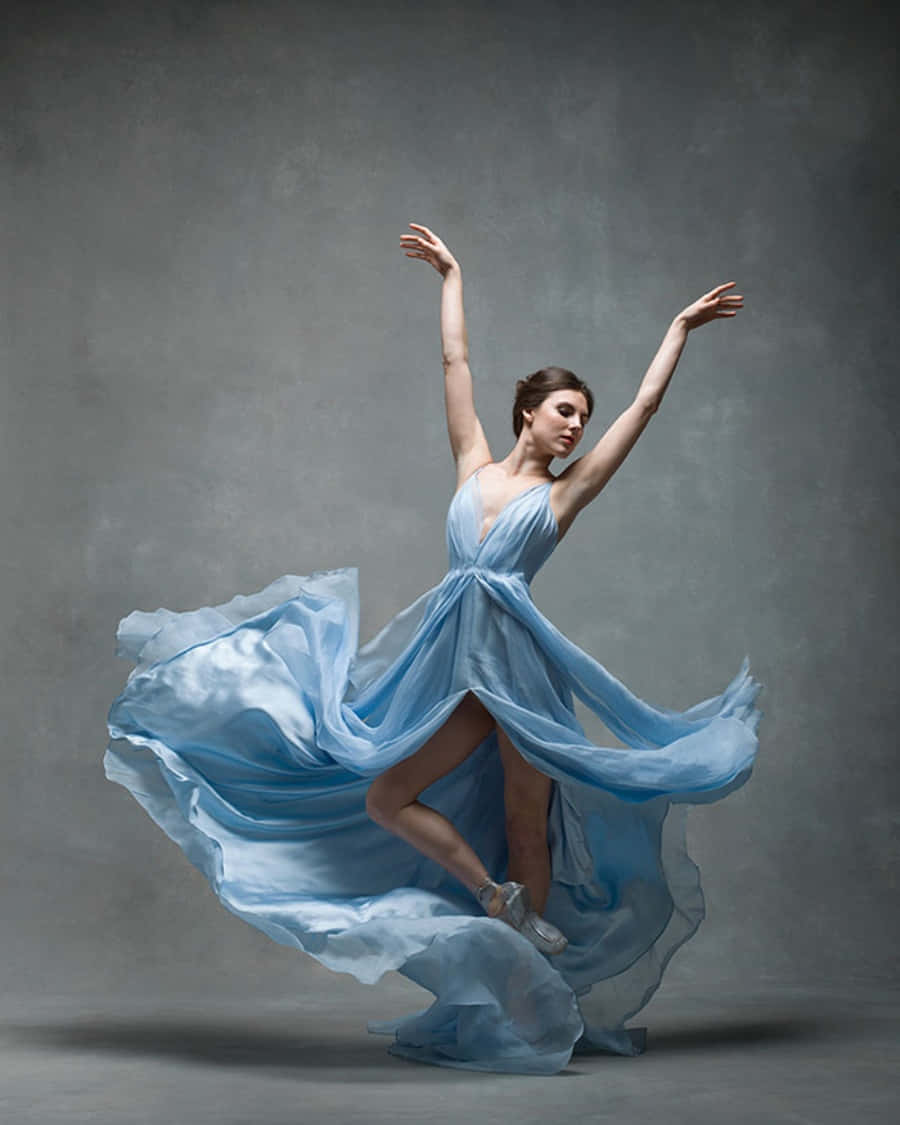 dancer 桌布 壁紙 — 一位優雅的芭蕾舞者穿著飄逸的淺藍色連衣裙，在柔和的灰色工作室背景前空中旋轉。