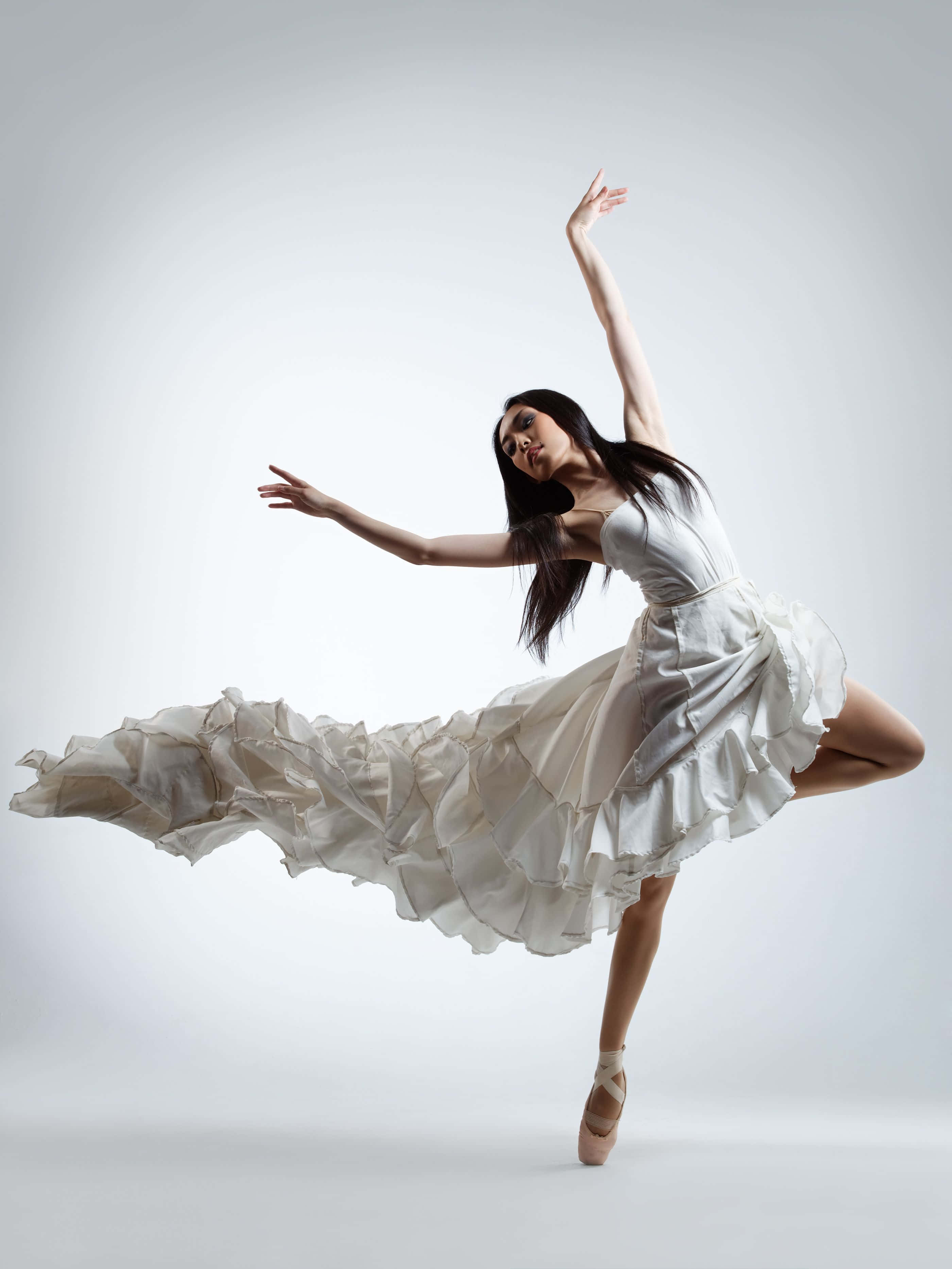 dancer 桌布 壁紙 — 一位優雅的芭蕾舞者穿著飄逸的白色連衣裙，在柔和的灰色工作室背景前騰空躍起。