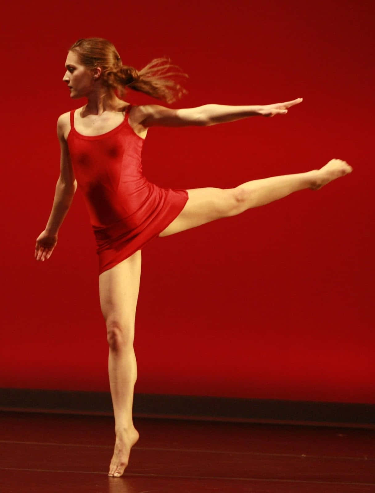 dancer 桌布 壁紙 — 一位優雅的芭蕾舞者身穿紅色緊身衣，在鮮紅色背景下於舞台上表演高踢腿。