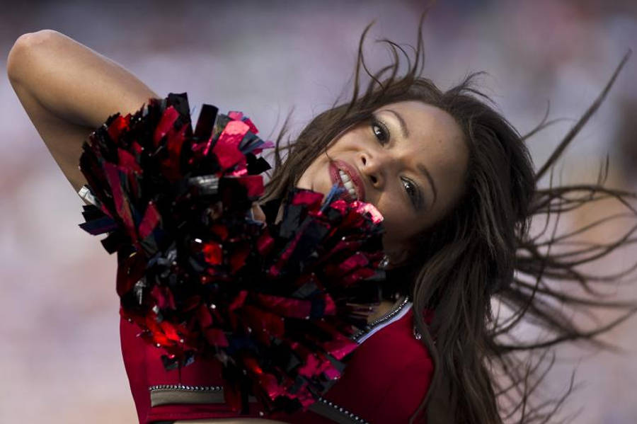Cheerleader 桌布 壁紙 — 一位充滿活力的啦啦隊員身穿紅色制服，手持黑色和紅色的絨球，在充滿活力的表演中頭髮飛揚，面帶微笑。