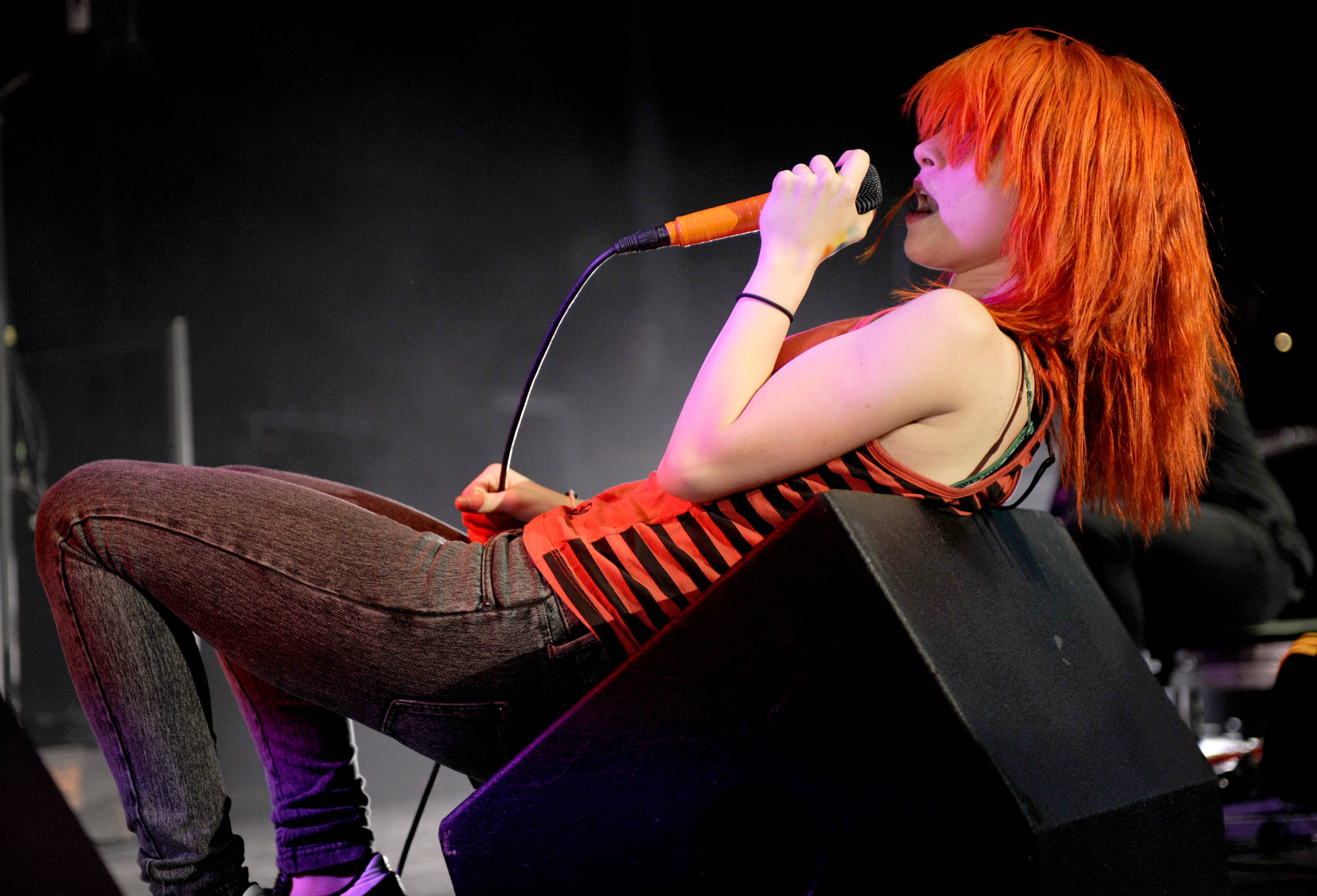 Hayley Williams 桌布 壁紙 — 一位充滿活力的橙髮歌手在舞台上熱情演出，靠著揚聲器並握著麥克風。