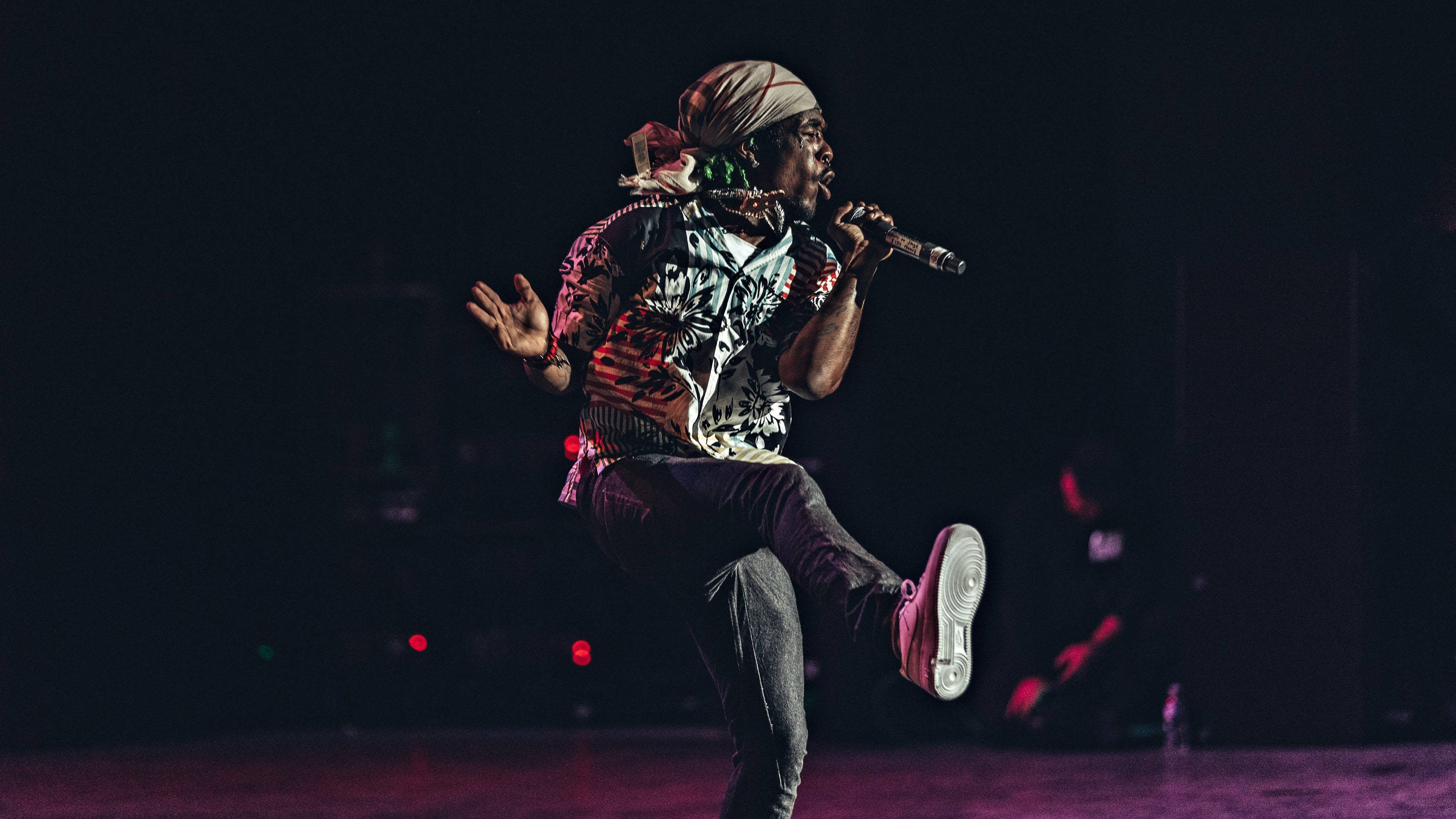 Lil Uzi Desktop 桌布 壁紙 — 一位充滿活力的表演者在舞台上騰空，手持麥克風，被戲劇性的紫色和紅色舞台燈光照亮，背景為深色。