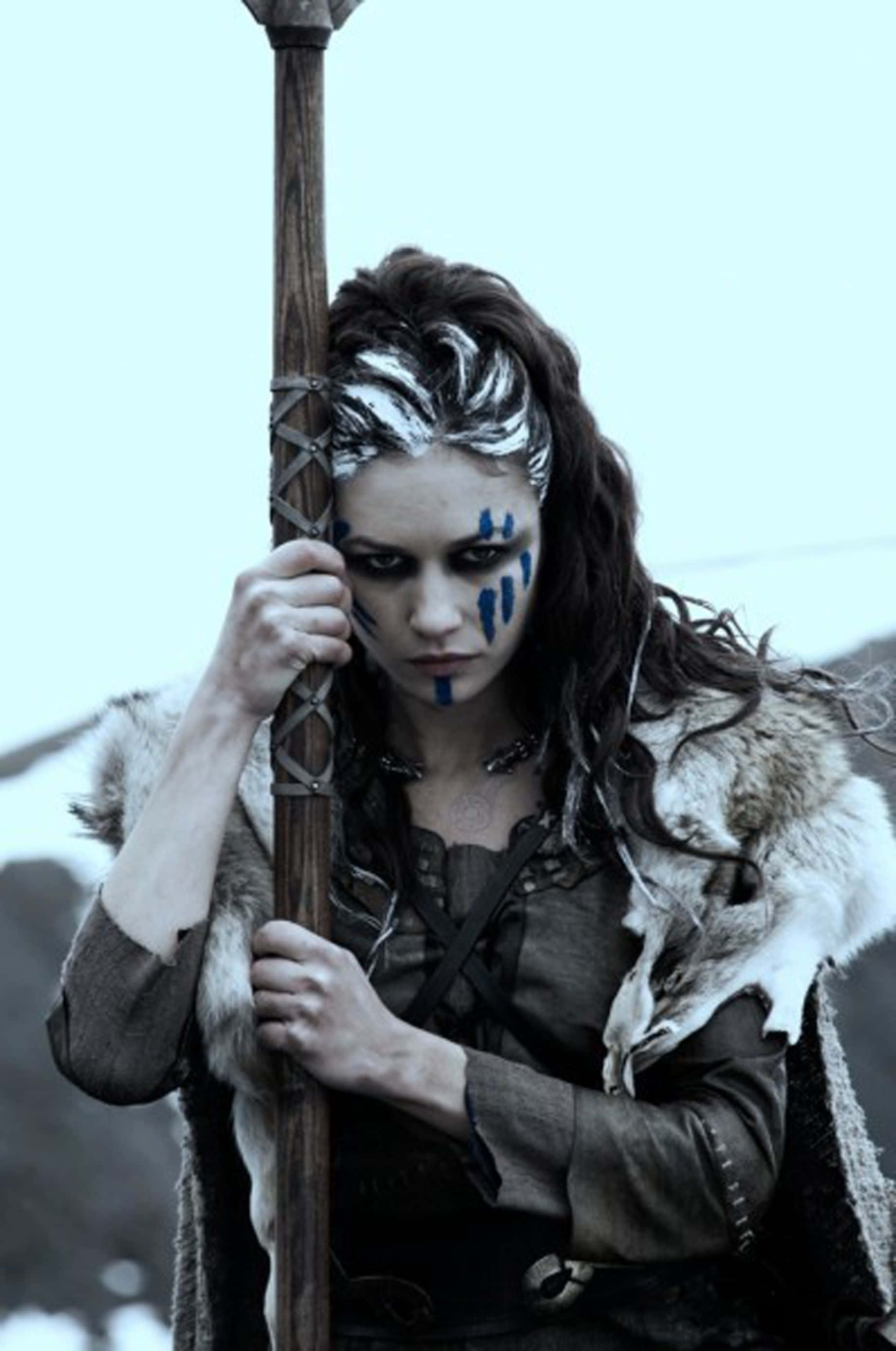 Female Viking Warriors 桌布 壁紙 — 一位兇猛的女戰士，臉上塗著藍色顏料，身穿毛皮鑲邊的盔甲，在雪景背景下握著一根木杖。