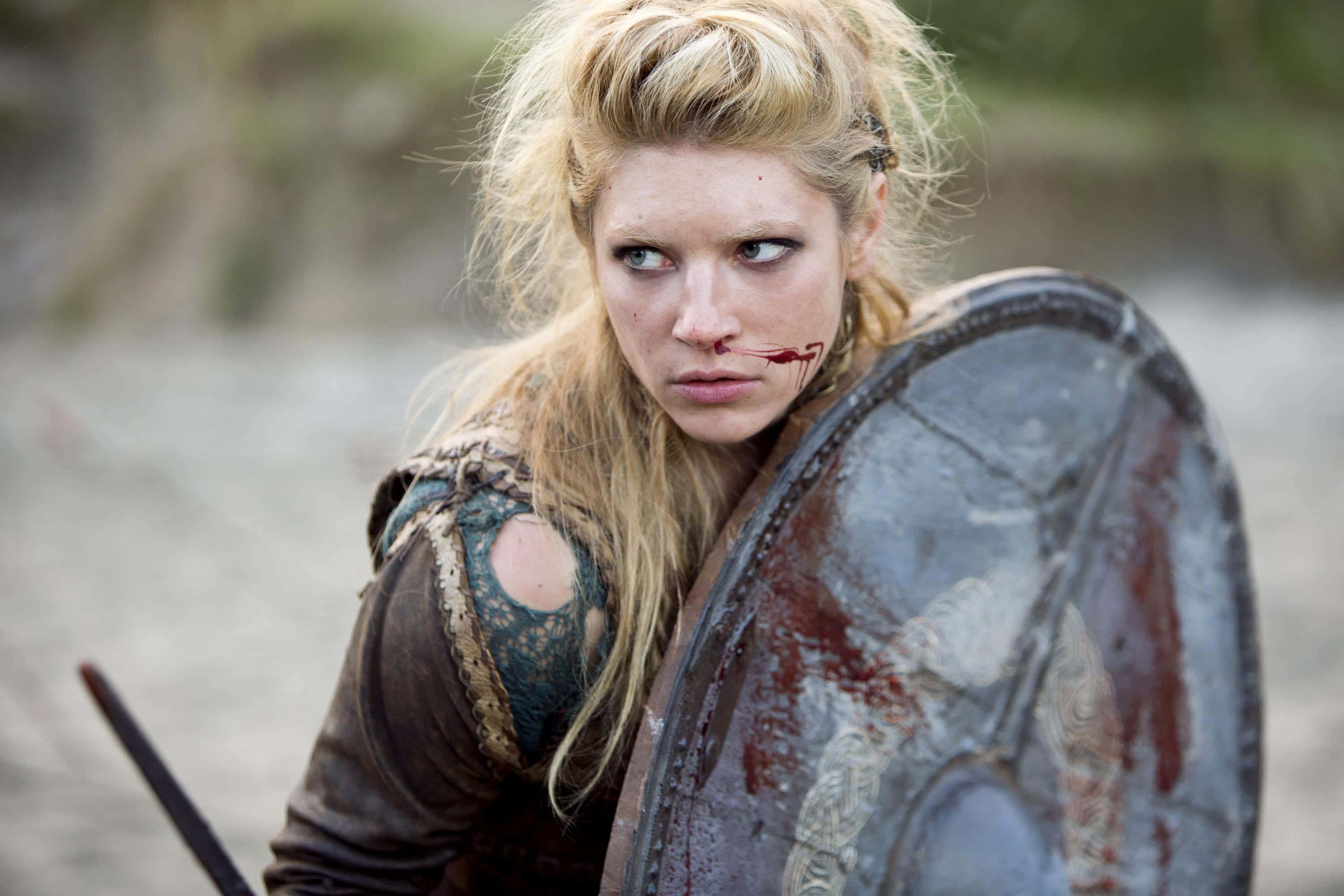 Female Viking Warriors 桌布 壁紙 — 一位兇猛的女戰士，臉上沾滿鮮血，手持盾牌，在戰火摧殘的森林空地中準備就緒。