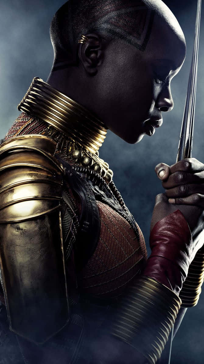 Okoye 桌布 壁紙 — 一位兇猛的戰士身穿華麗金色盔甲，在煙霧瀰漫的黑暗背景下，手持劍，表情莊嚴。