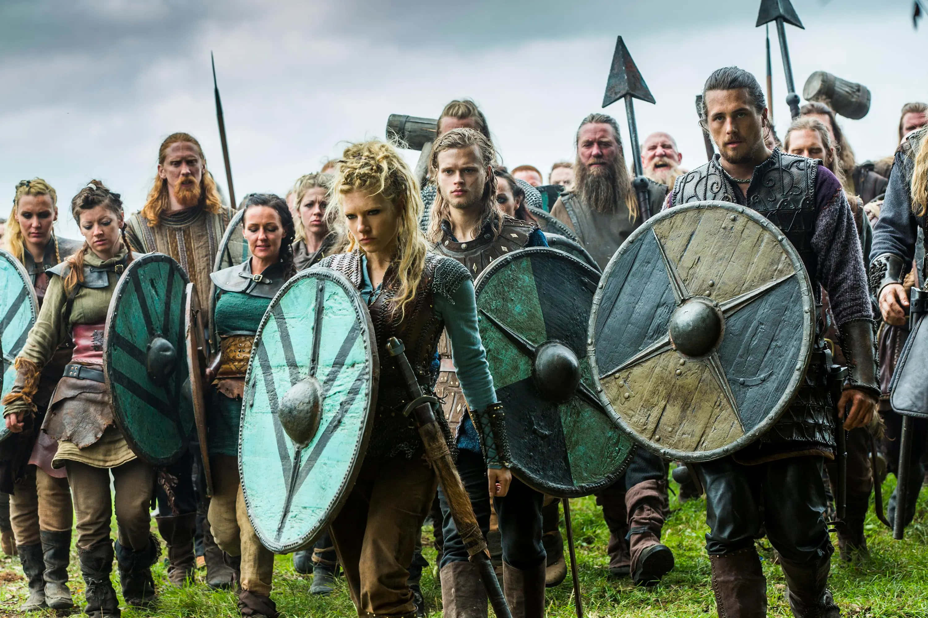 Female Viking Warriors 桌布 壁紙 — 一位兇猛的維京女戰士帶領一個準備戰鬥的部族，手持木盾和長矛，在陰雲密布的天空下。