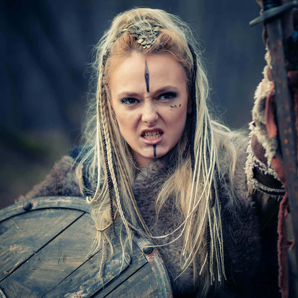 Female Viking Warriors 桌布 壁紙 — 一位兇猛的金髮女戰士，臉上塗有顏料並編著辮子，在霧氣瀰漫的森林中緊握木盾。