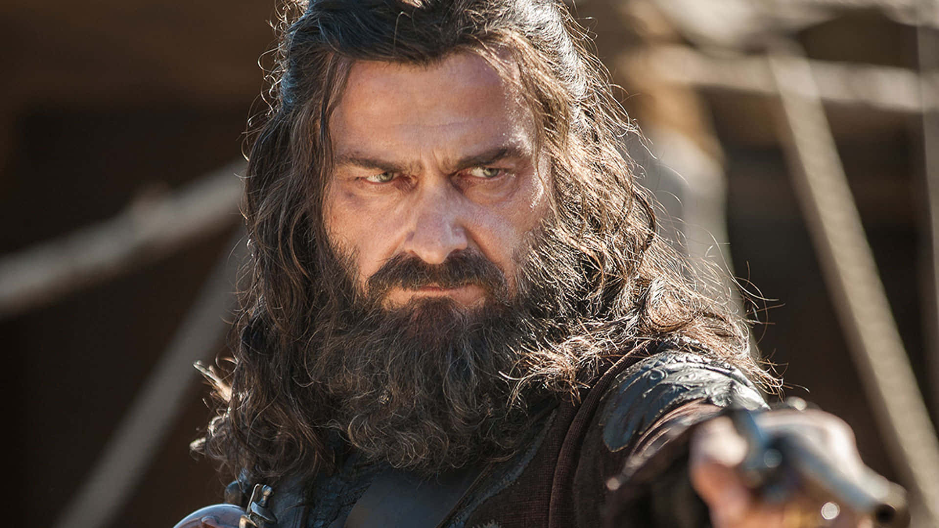 Ray Stevenson 桌布 壁紙 — 一位兇猛的鬍鬚戰士，眼神凌厲，在陽光照耀的木船場景中緊握一把劍。
